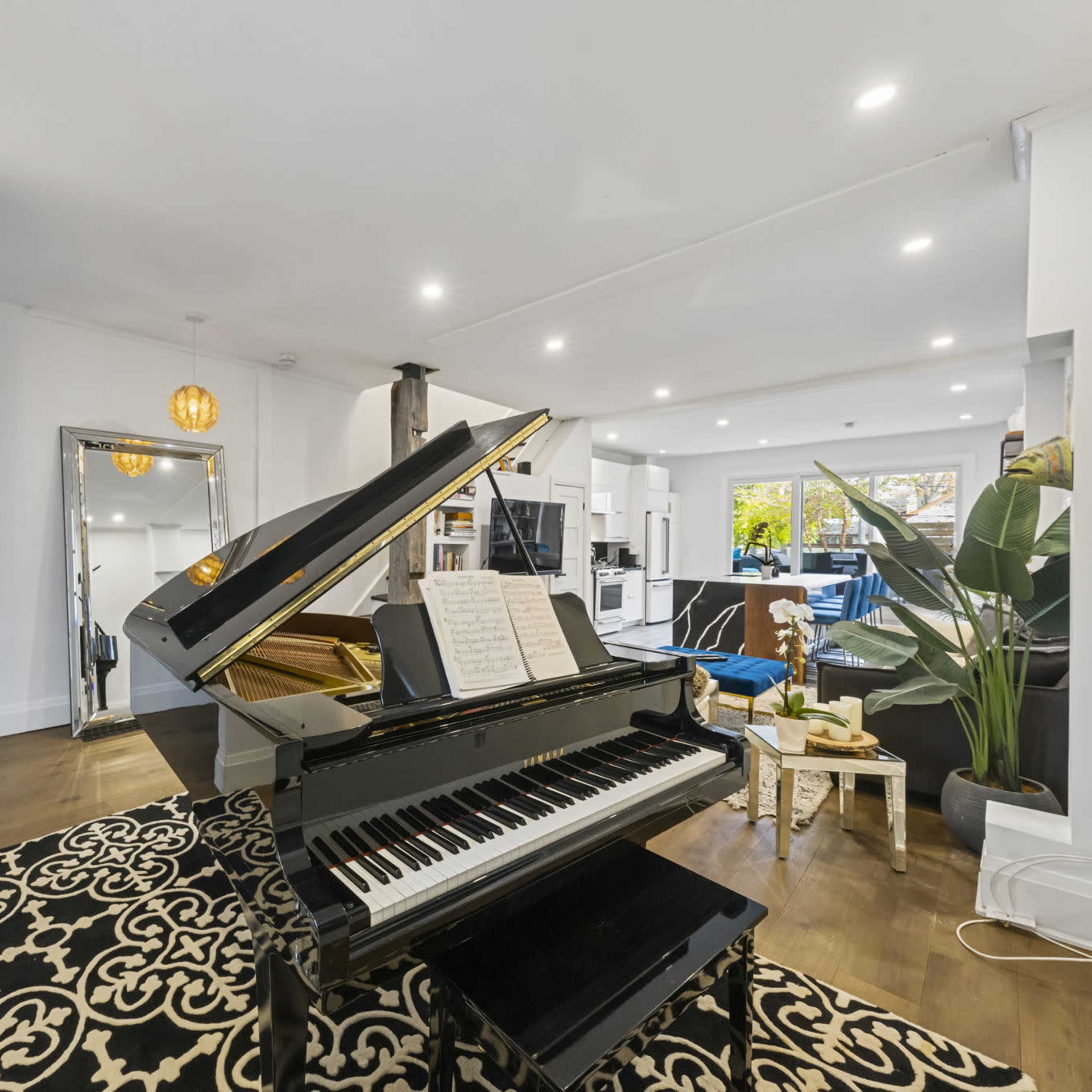 A grand piano sits in the foreground of a bright living room featuring modern furniture and decor.