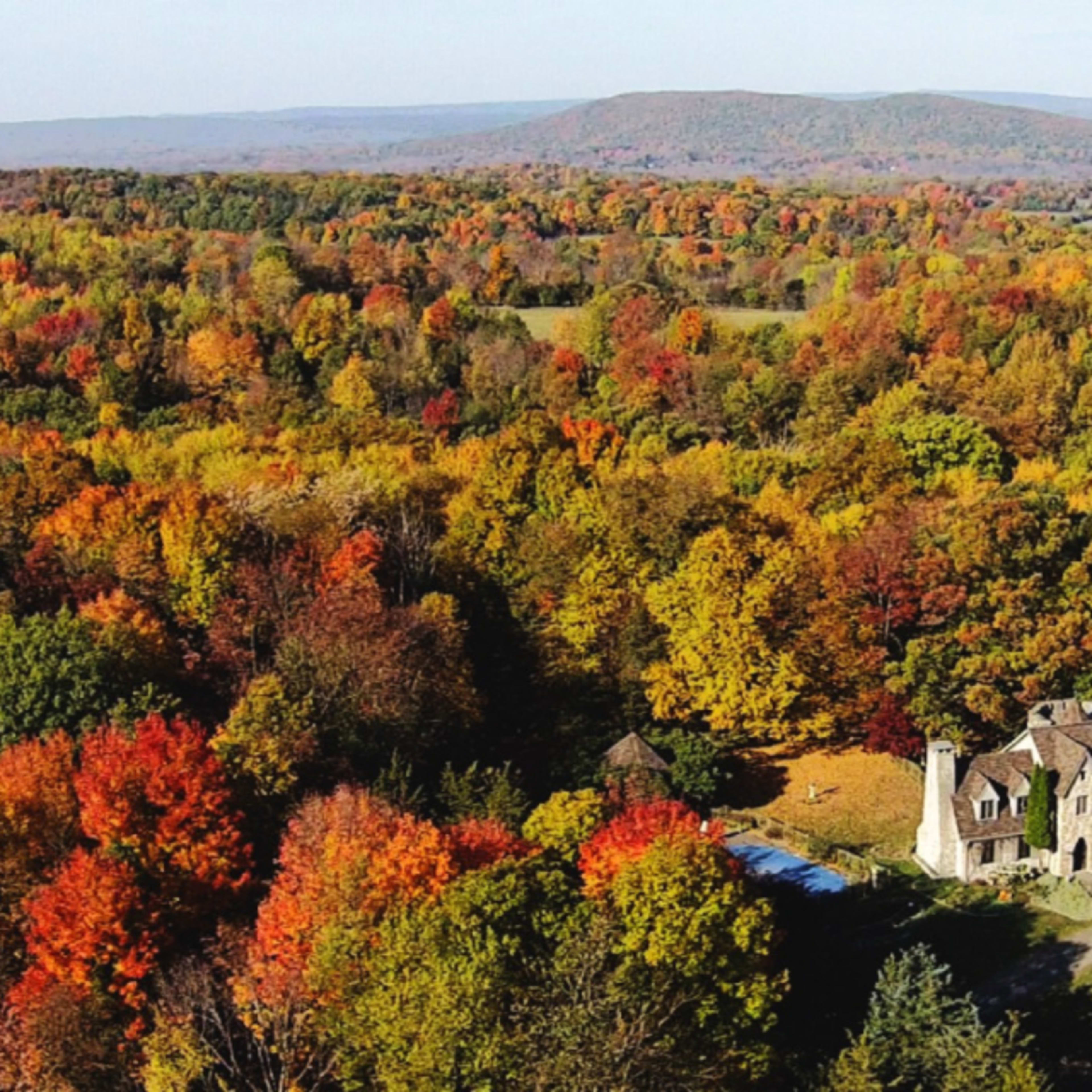 A stone mansion surrounded by vibrant fall foliage and rolling hills.