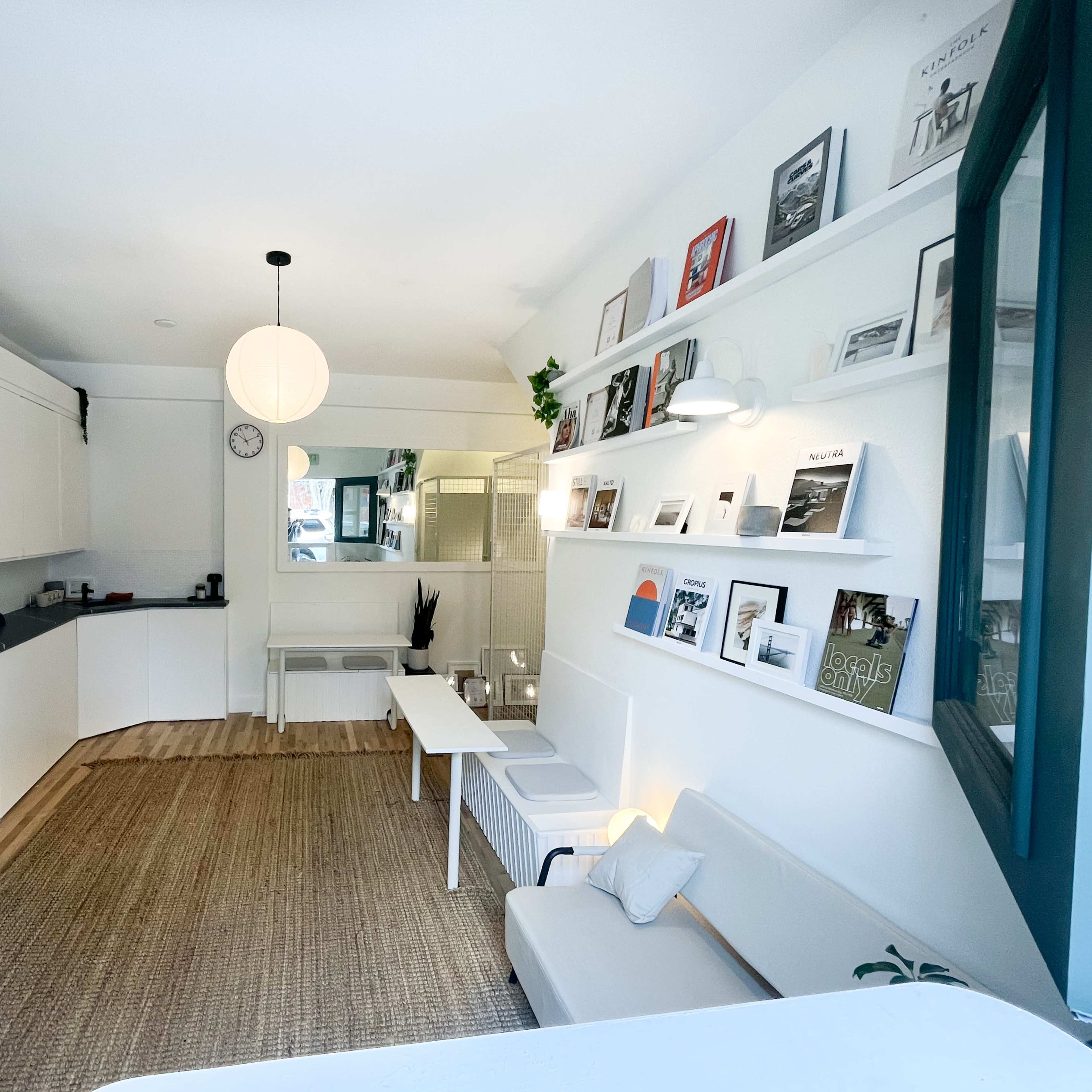 A cozy interior space with a white sofa, a spacious kitchen area, a circular pendant light, and shelves displaying framed pictures.