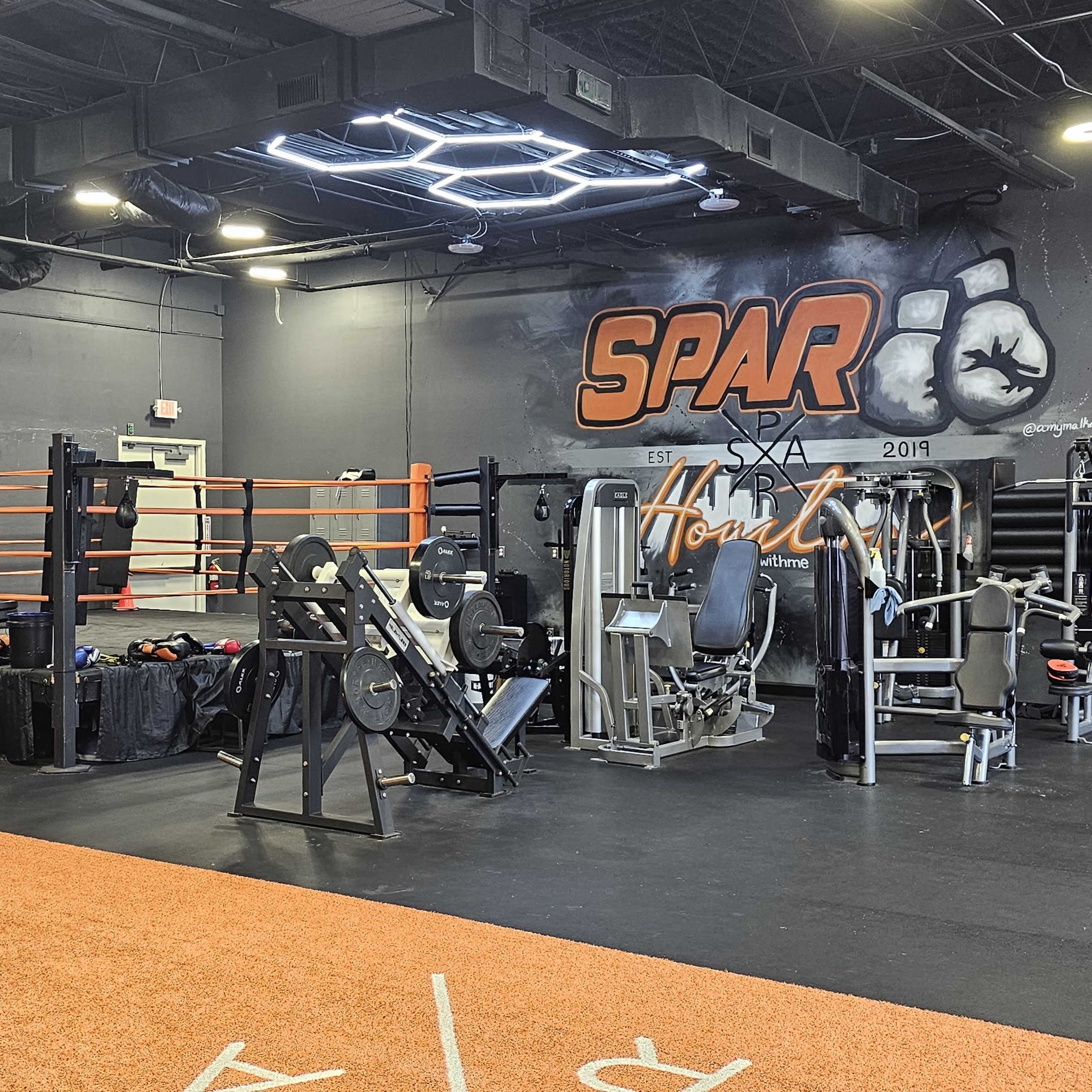 A boxing and fitness gym with a ring, various workout machines, and a vibrant mural on the wall.
