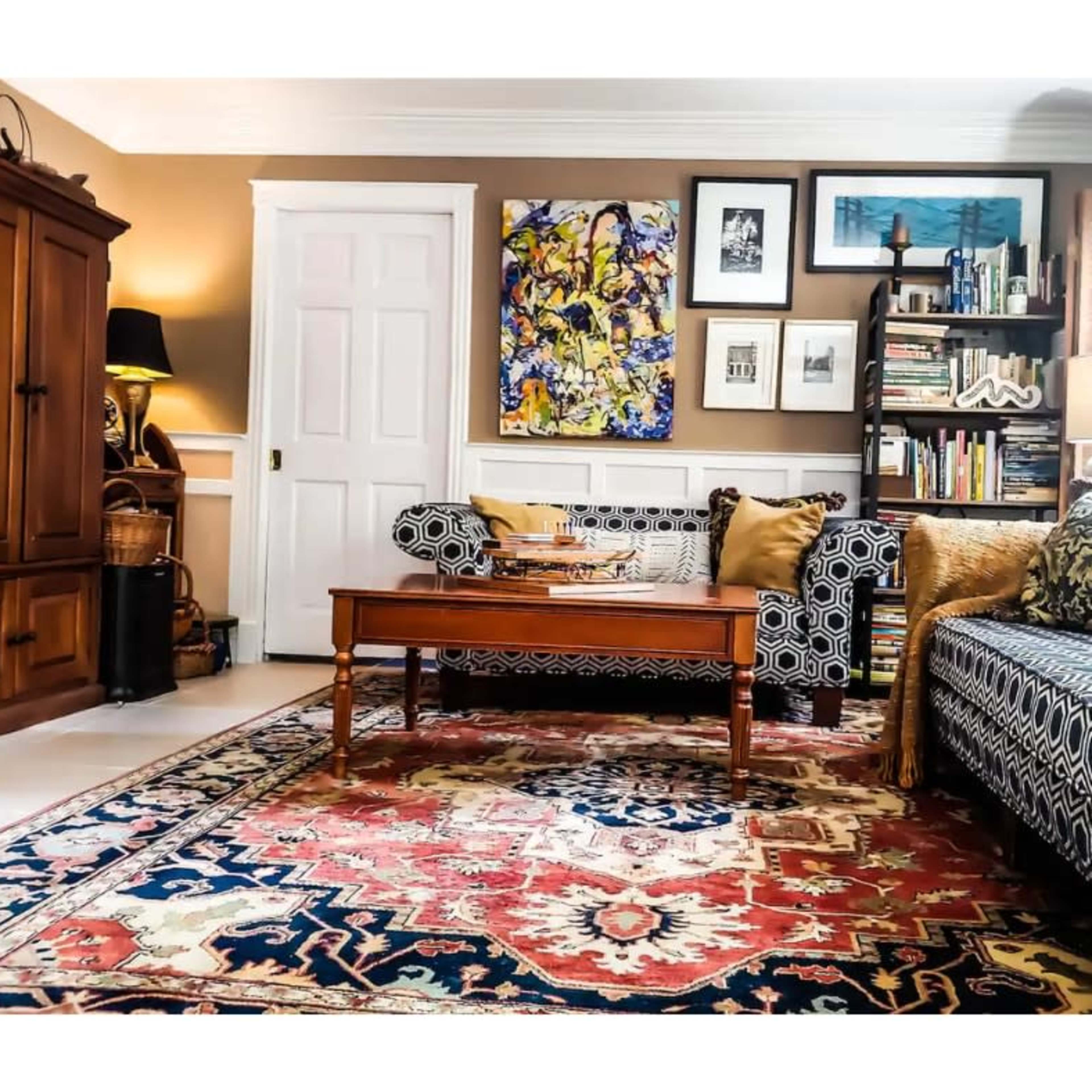 The living room features two patterned sofas, a wooden coffee table, a colorful rug, and bookshelves filled with books and decor.