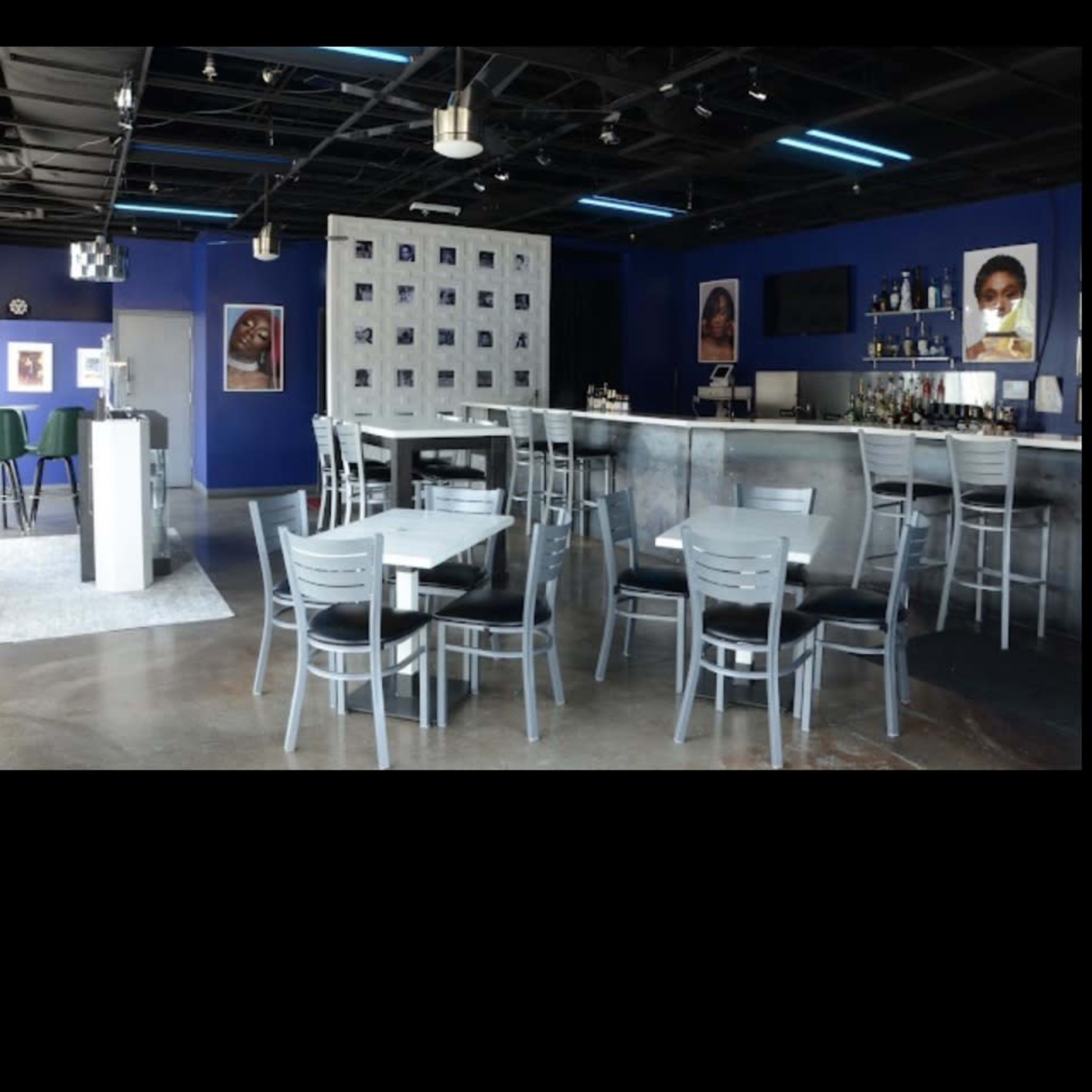 A modern restaurant interior with gray chairs and tables arranged around a bar area in a blue-walled space.