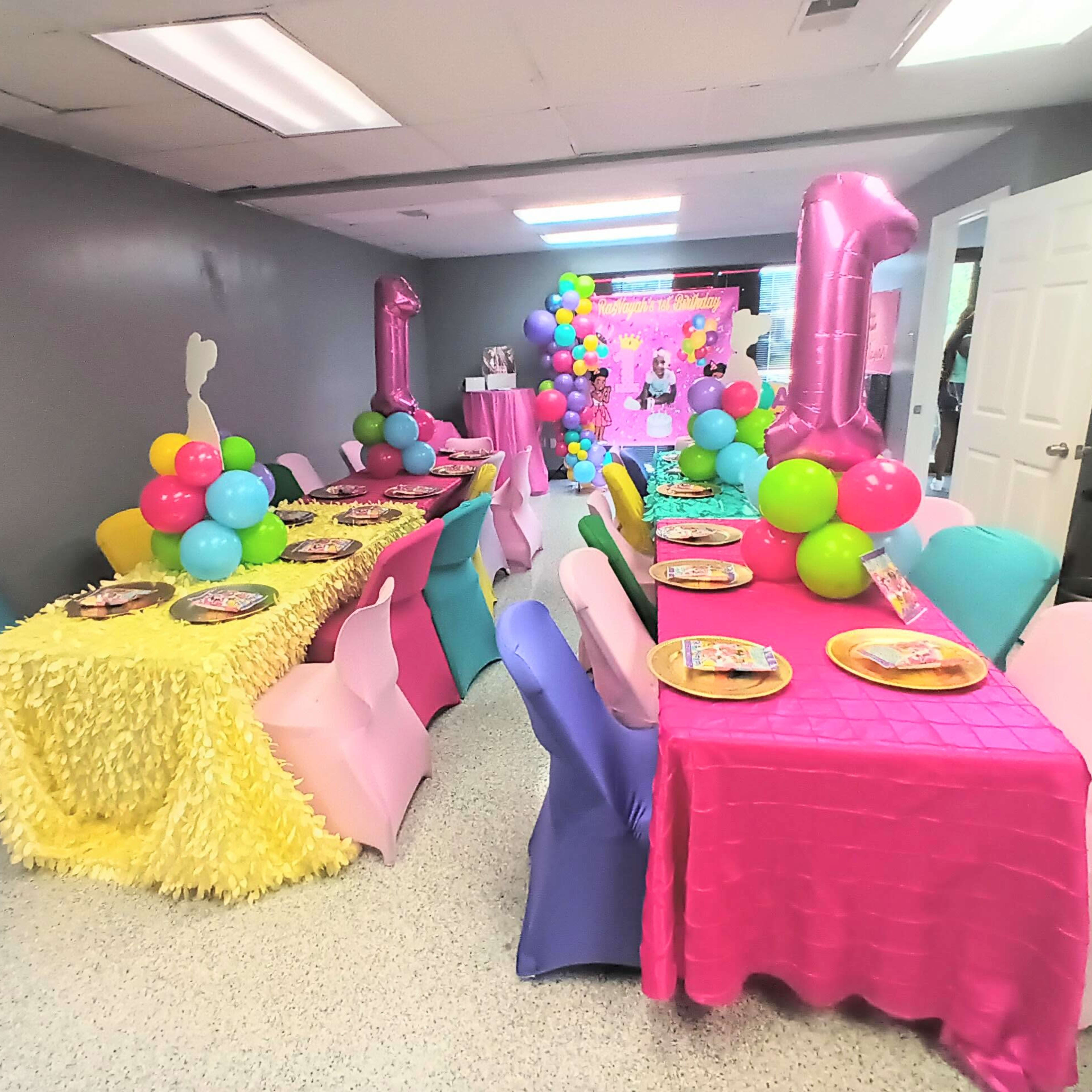 A festive party room features tables covered in colorful tablecloths adorned with balloons and themed decorations.