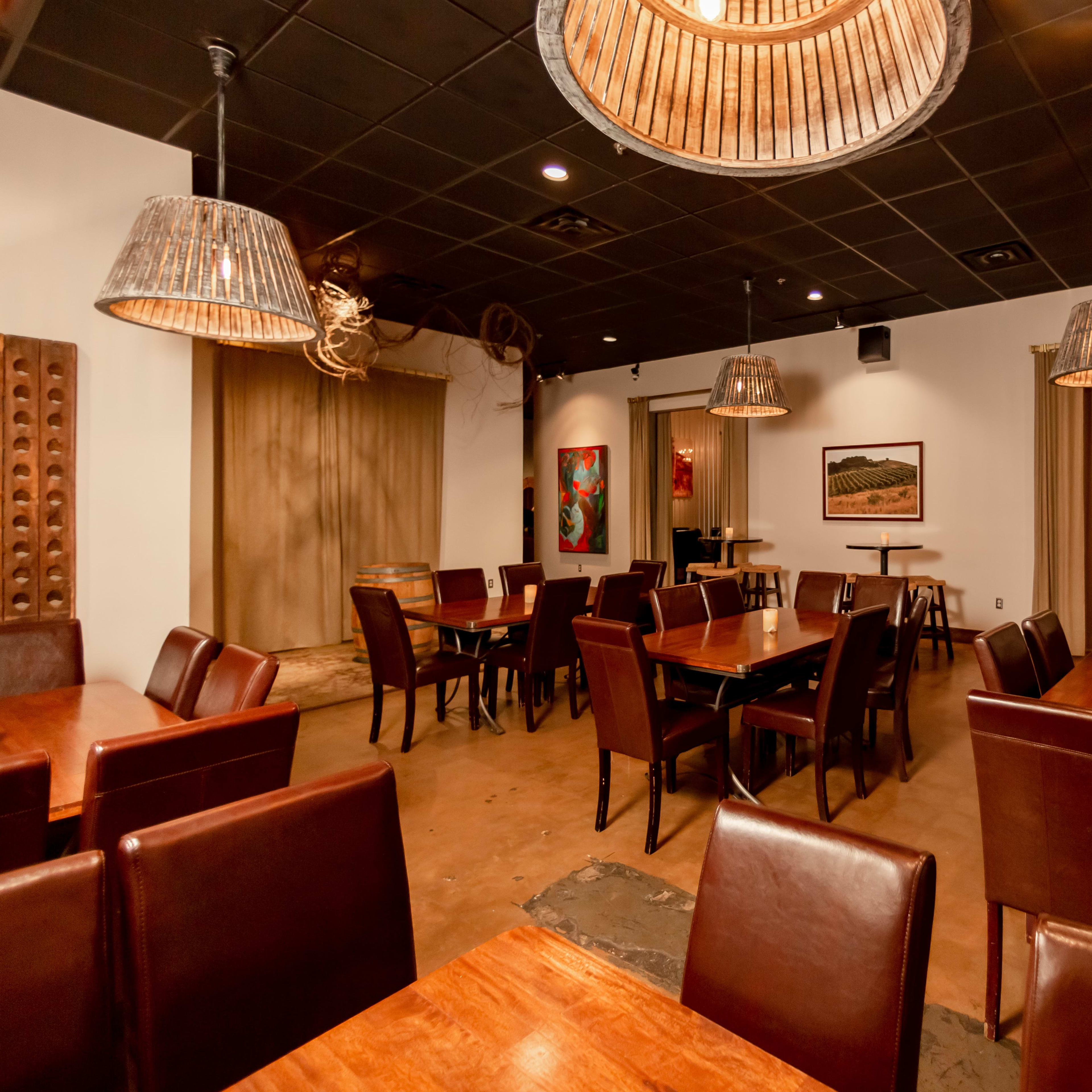 A spacious restaurant interior with wooden tables and chairs, woven pendant lights, and artwork on the walls.