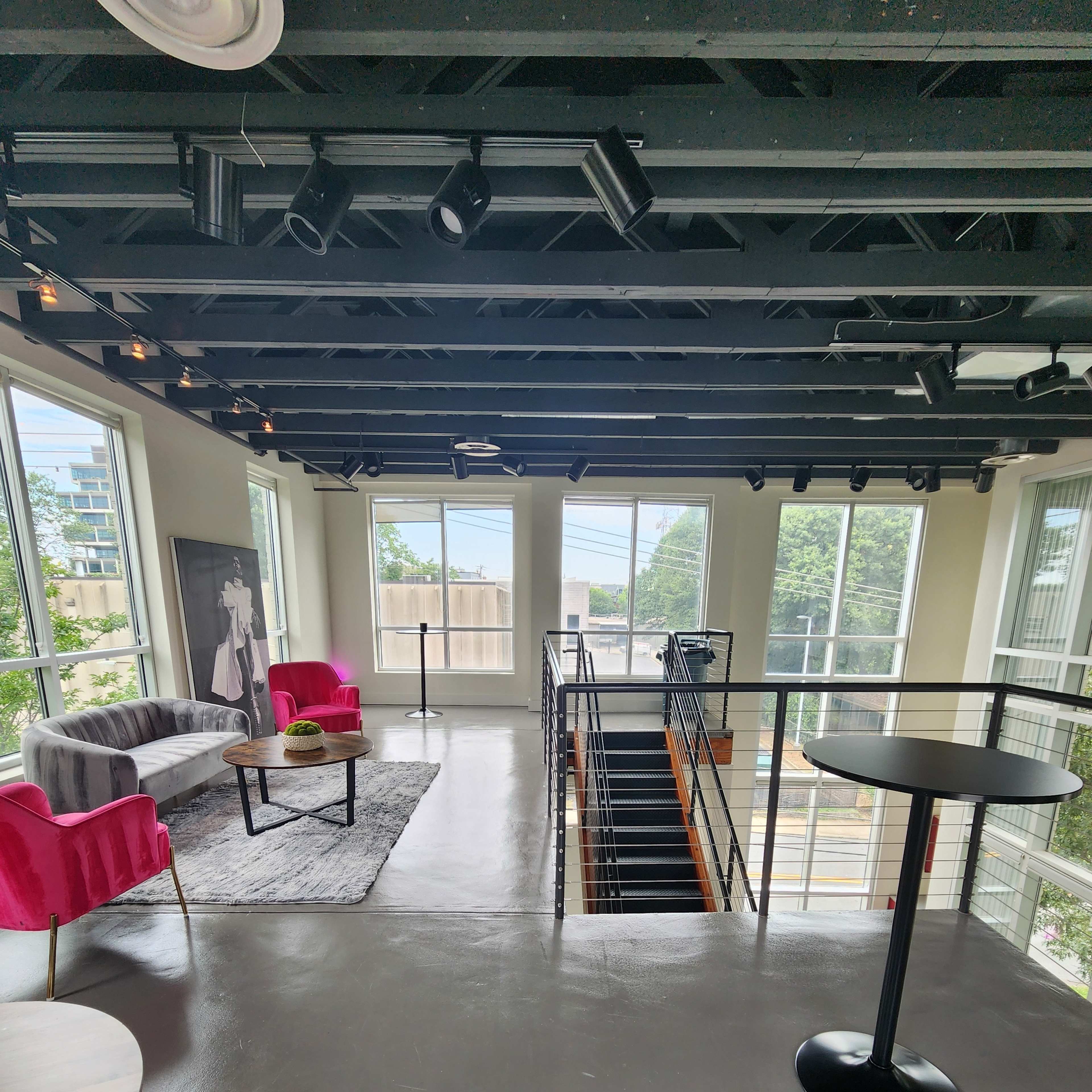 A large, well-lit room with modern furniture, including pink chairs, a coffee table, and a staircase leading to a lower level.