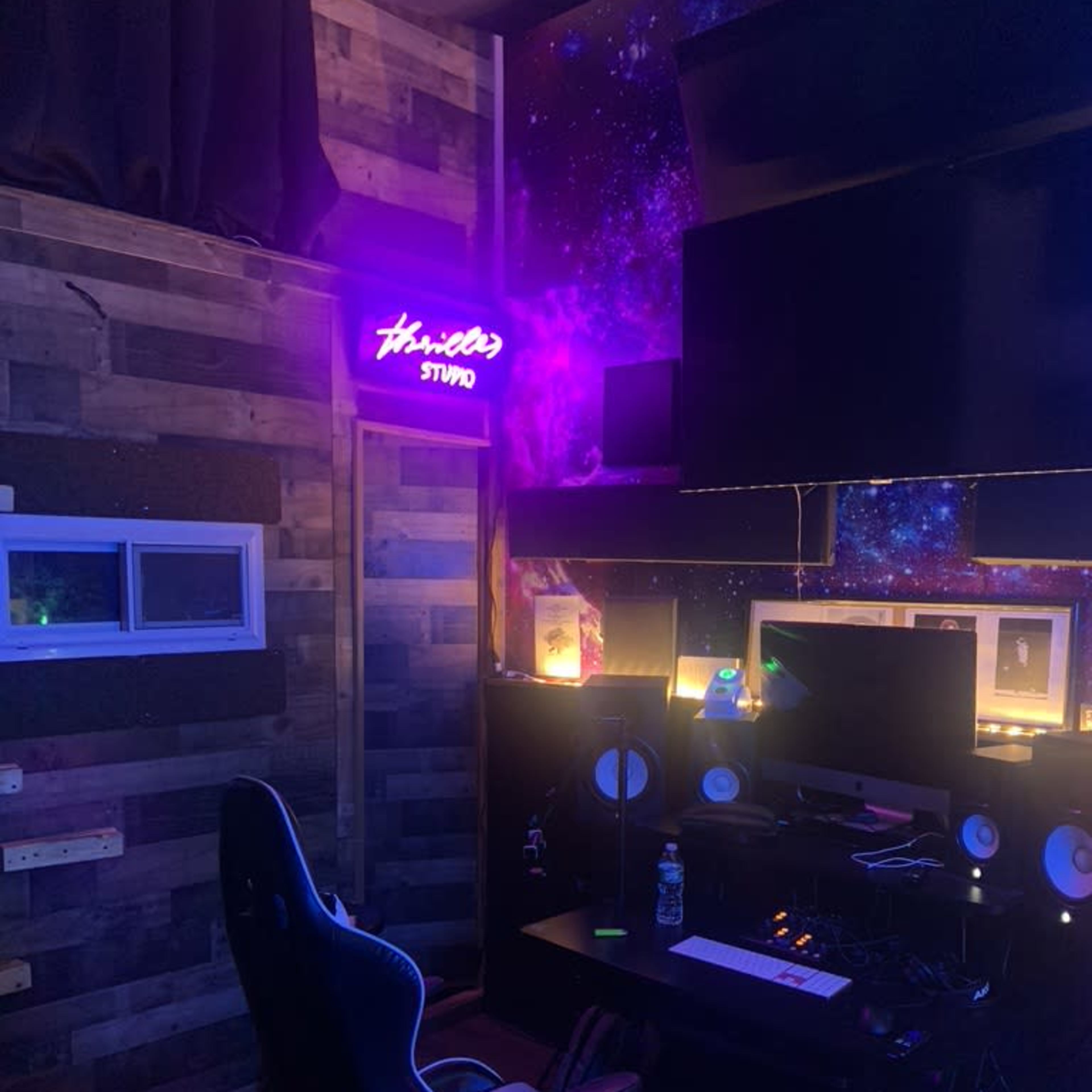 A music studio is shown with a dark wooden wall, purple lighting, and a desk equipped with audio equipment and a computer chair.