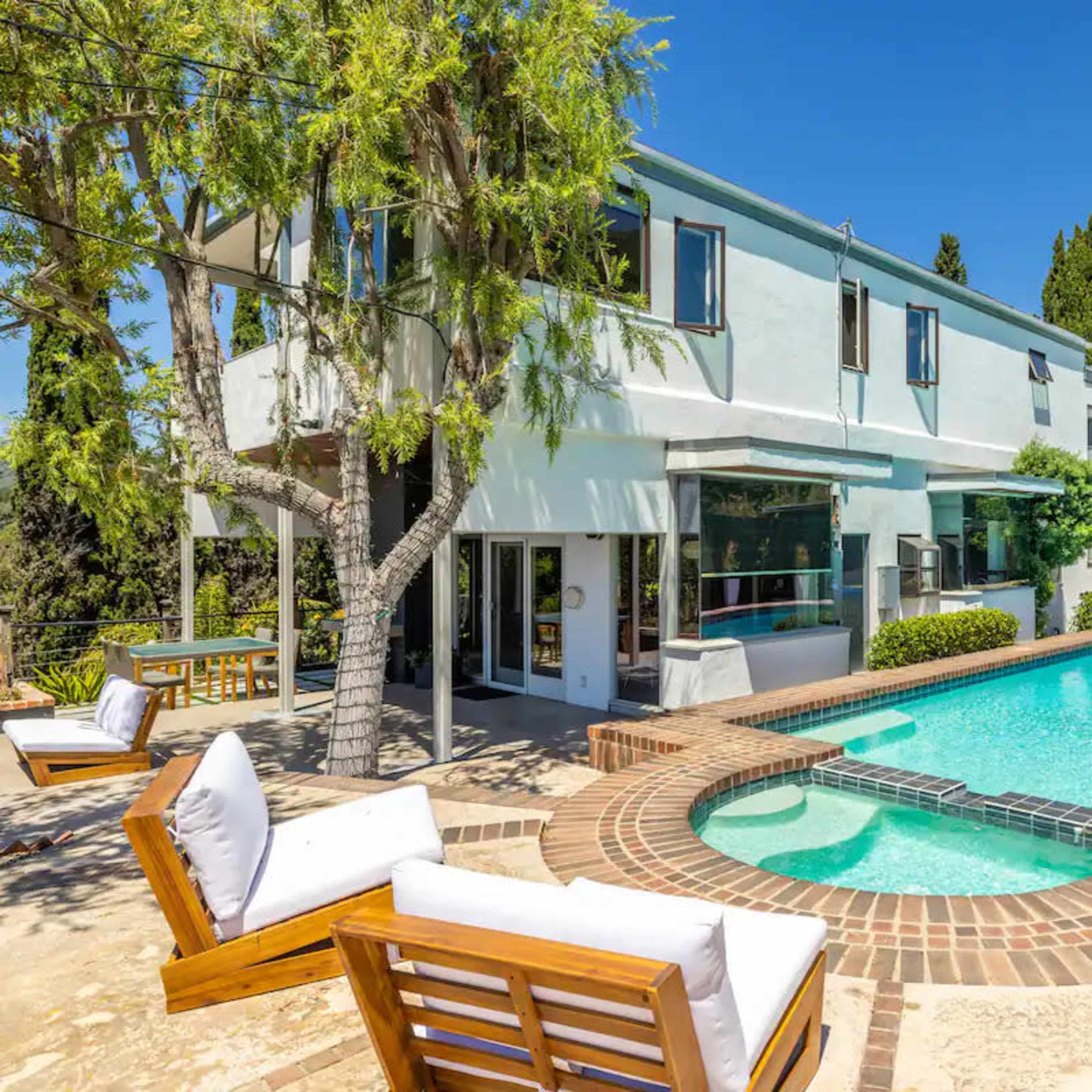 A modern house with an inviting swimming pool surrounded by landscaped greenery and outdoor seating.