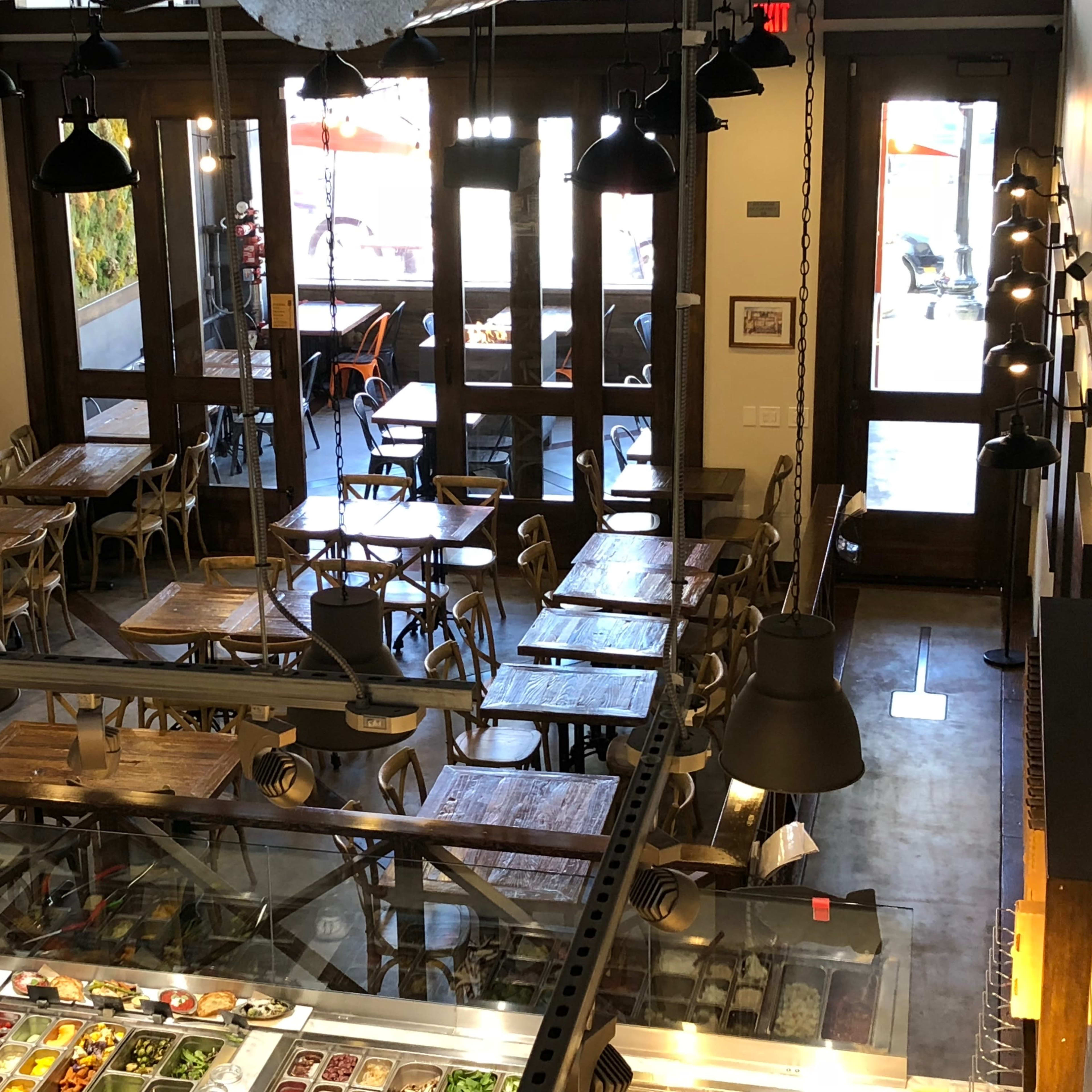 An overhead view of a cafe with wooden tables and chairs, featuring a large window and a screen displaying news.