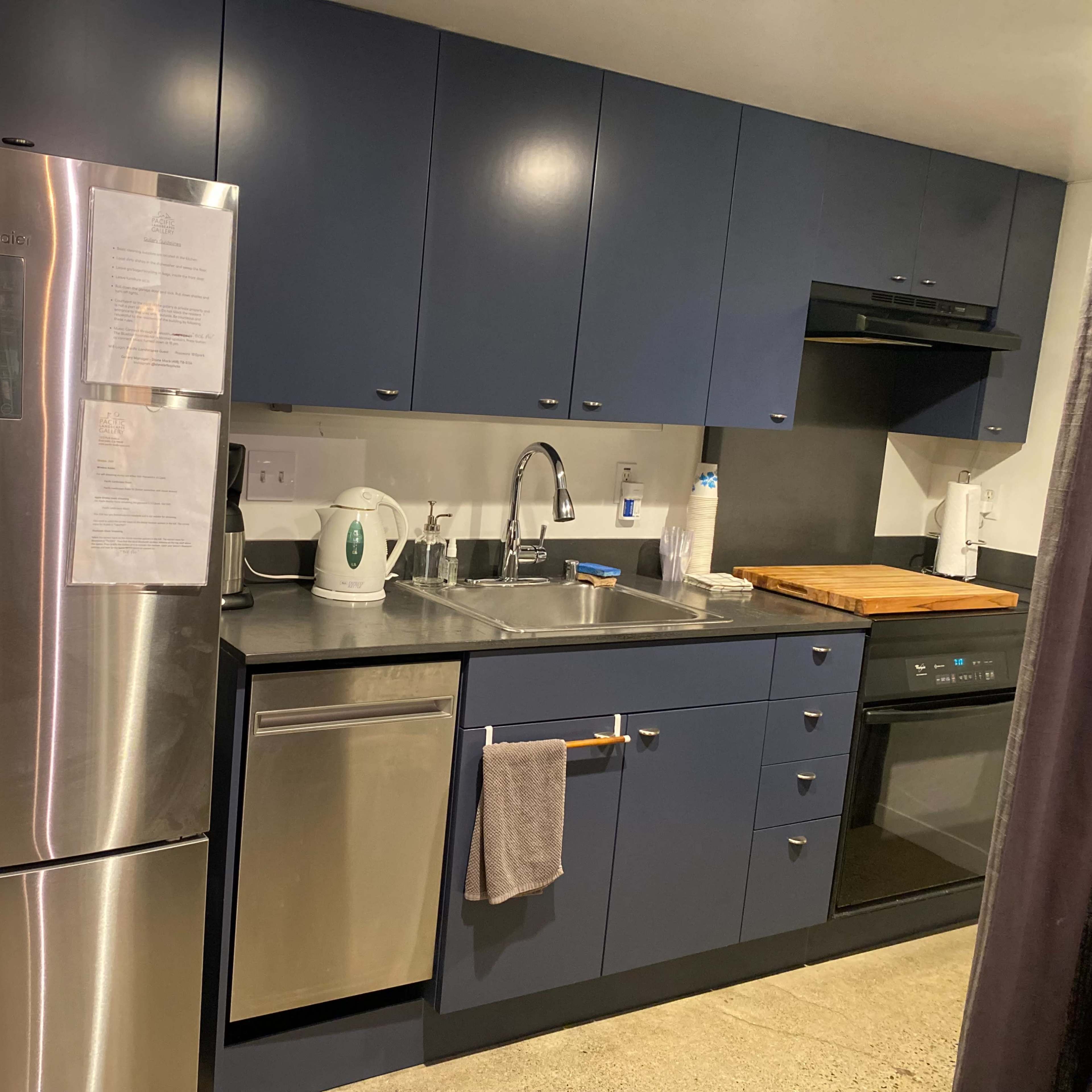 A modern kitchen features dark blue cabinets, stainless steel appliances, and a gray countertop with a cutting board.