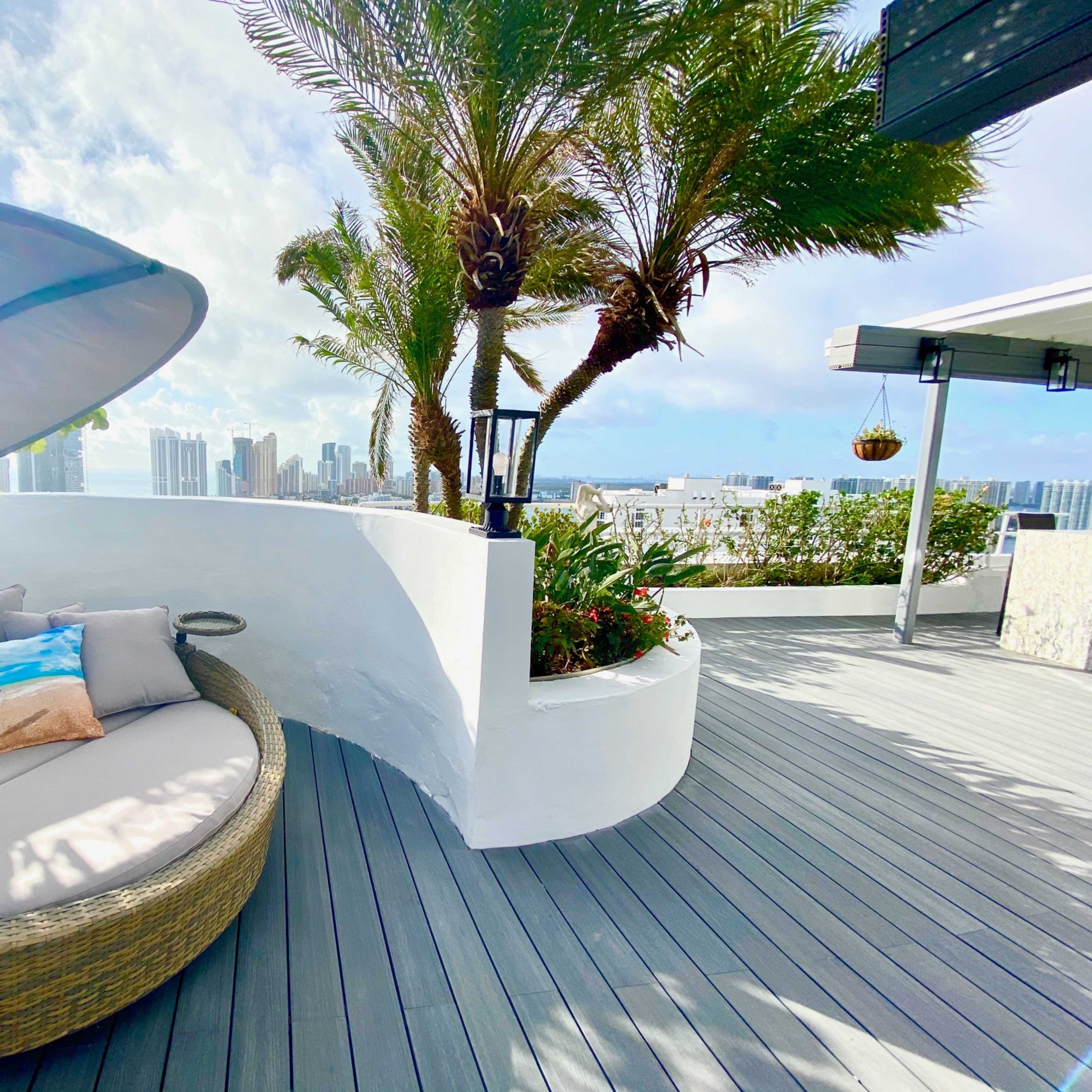 A round, cushioned seating area is set on a deck surrounded by palms and city skyline views.