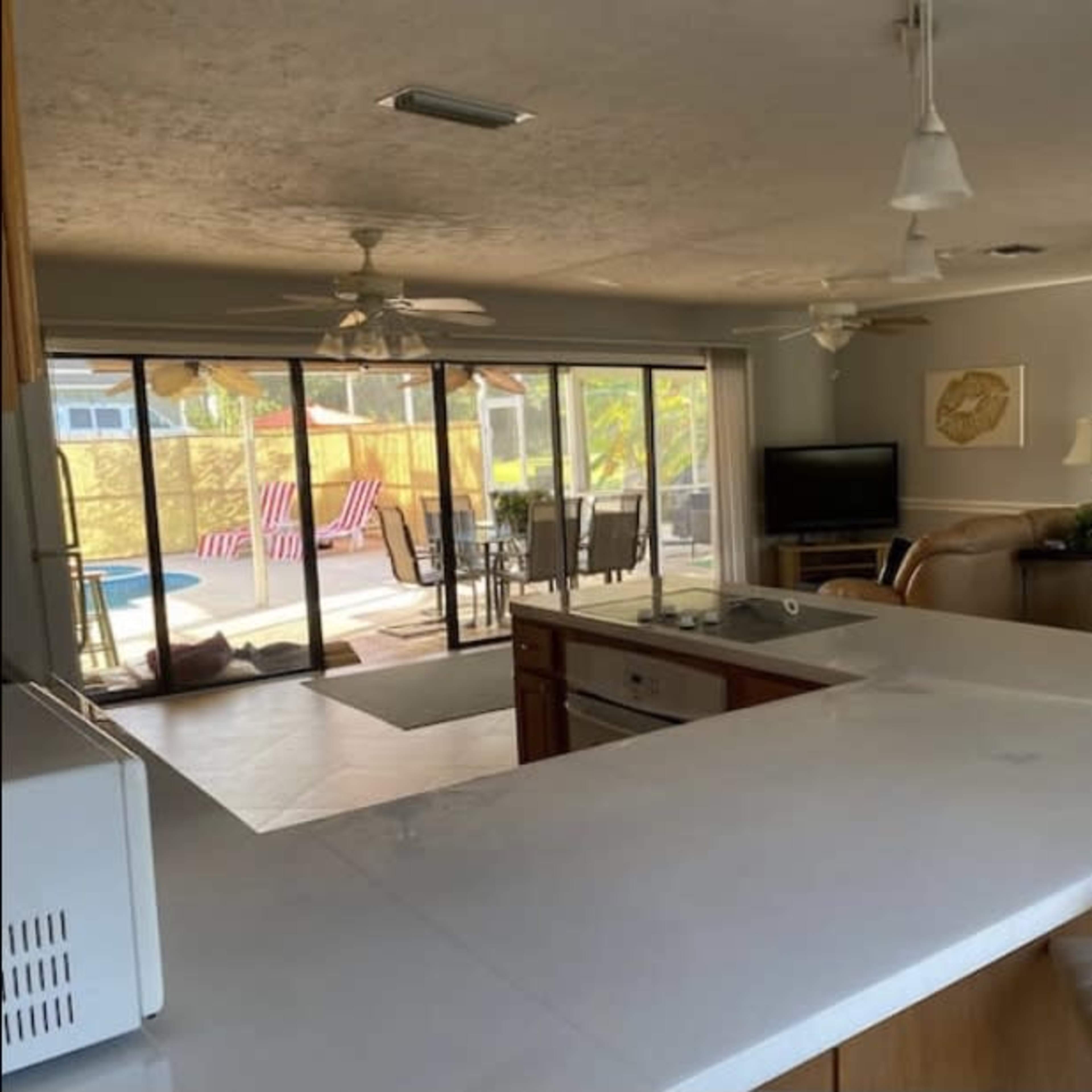 A spacious kitchen with a central island, open to a living area and a patio with outdoor furniture in the background.