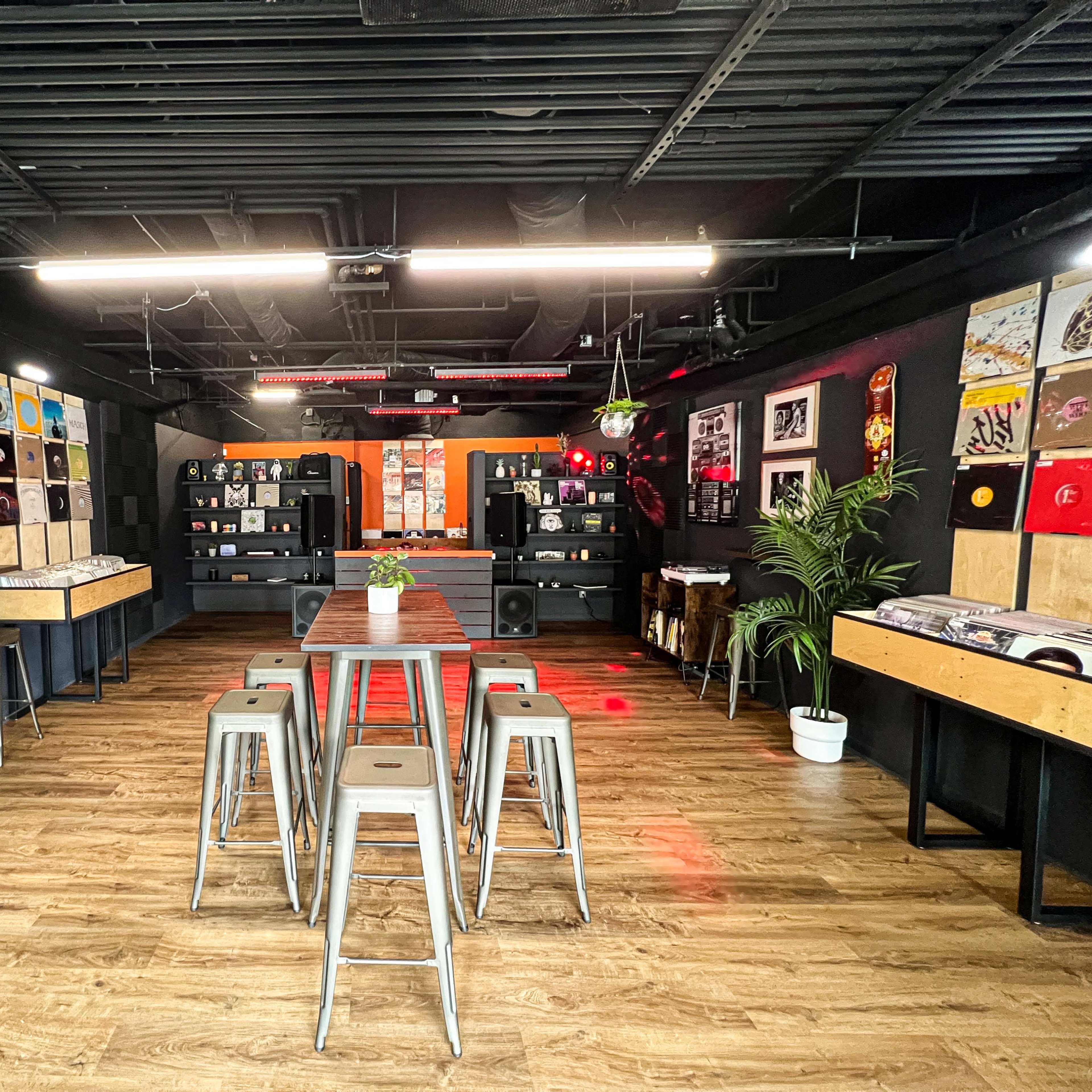 A modern shop featuring a display of vinyl records on the walls, a central table with metal stools, and a sleek, industrial interior design.