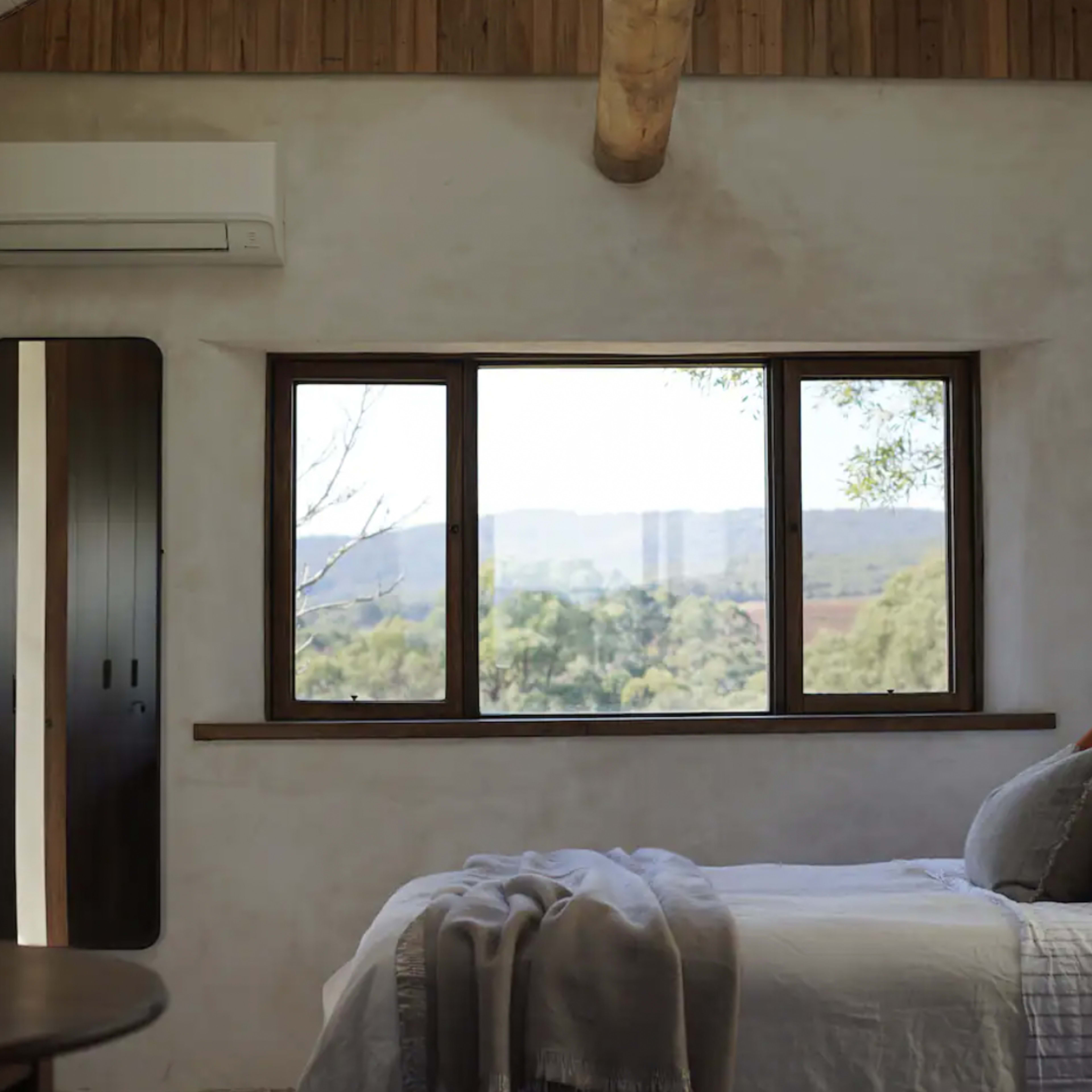 A cozy bedroom features a bed with pillows and a blanket, alongside a window offering a view of a scenic landscape.