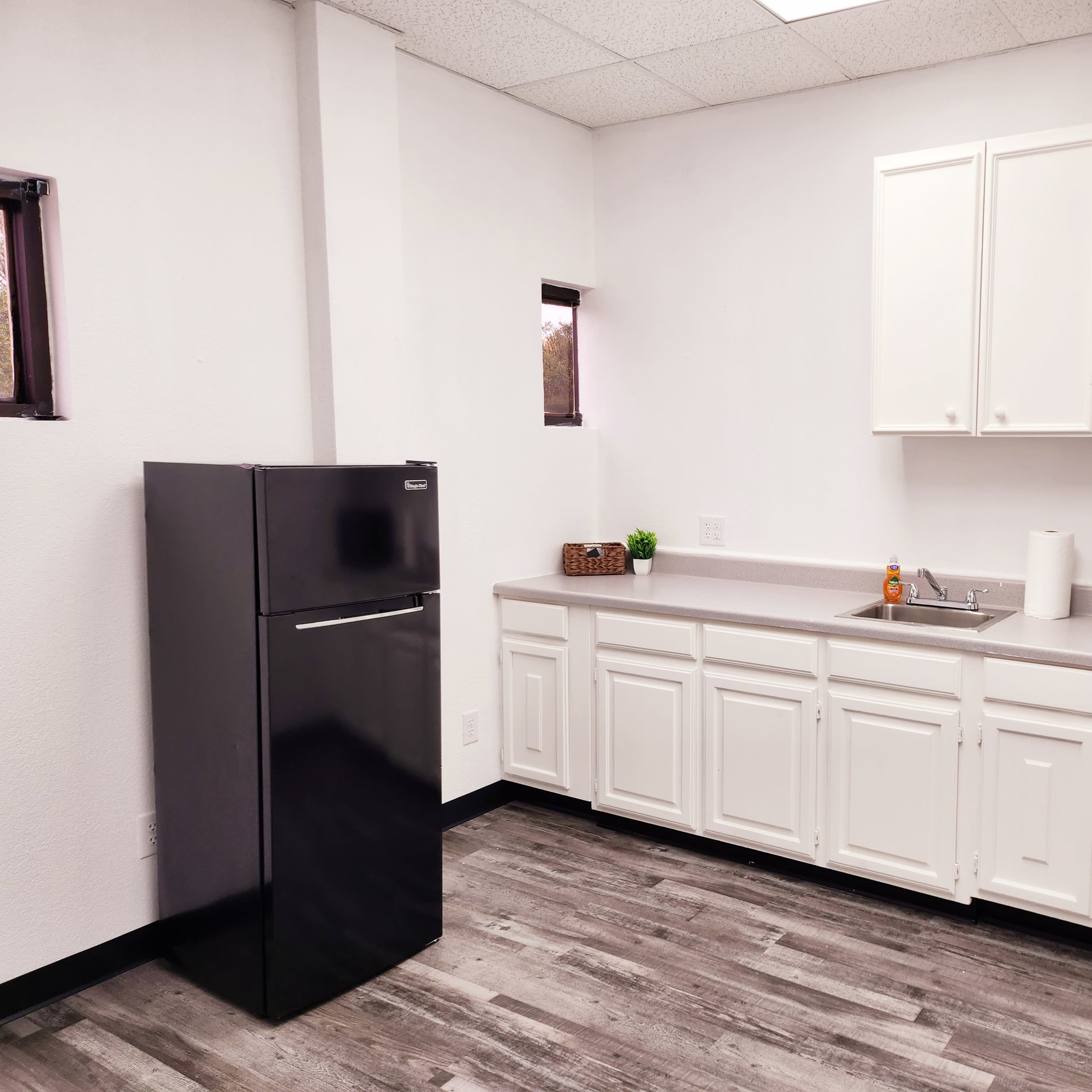 A kitchenette with a black refrigerator, white cabinetry, a sink, and a microwave on the counter.