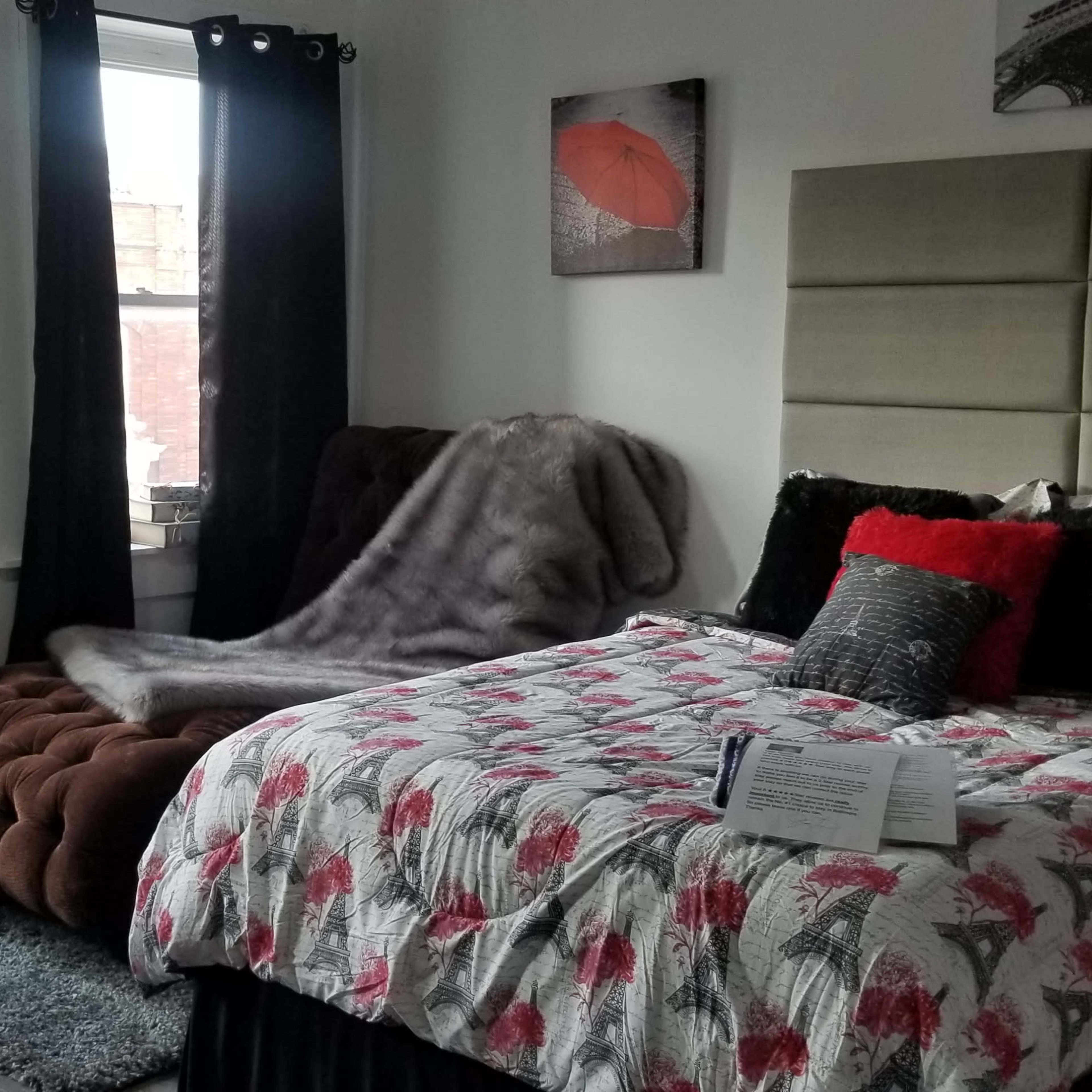 A bedroom with two beds, one with a patterned comforter and the other with a darker, solid cover, along with large windows and dark curtains.