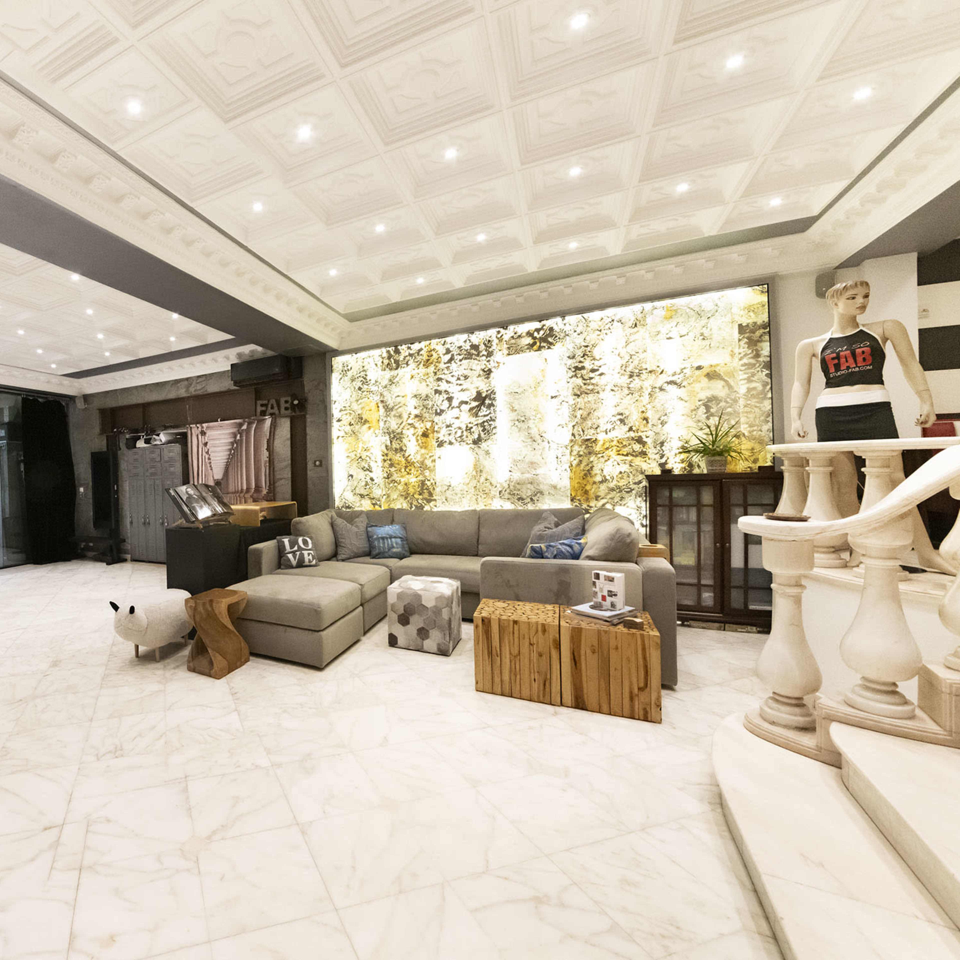 A spacious, modern interior with a marble floor, a large sectional sofa, and decorative wall features illuminated by ceiling lights.