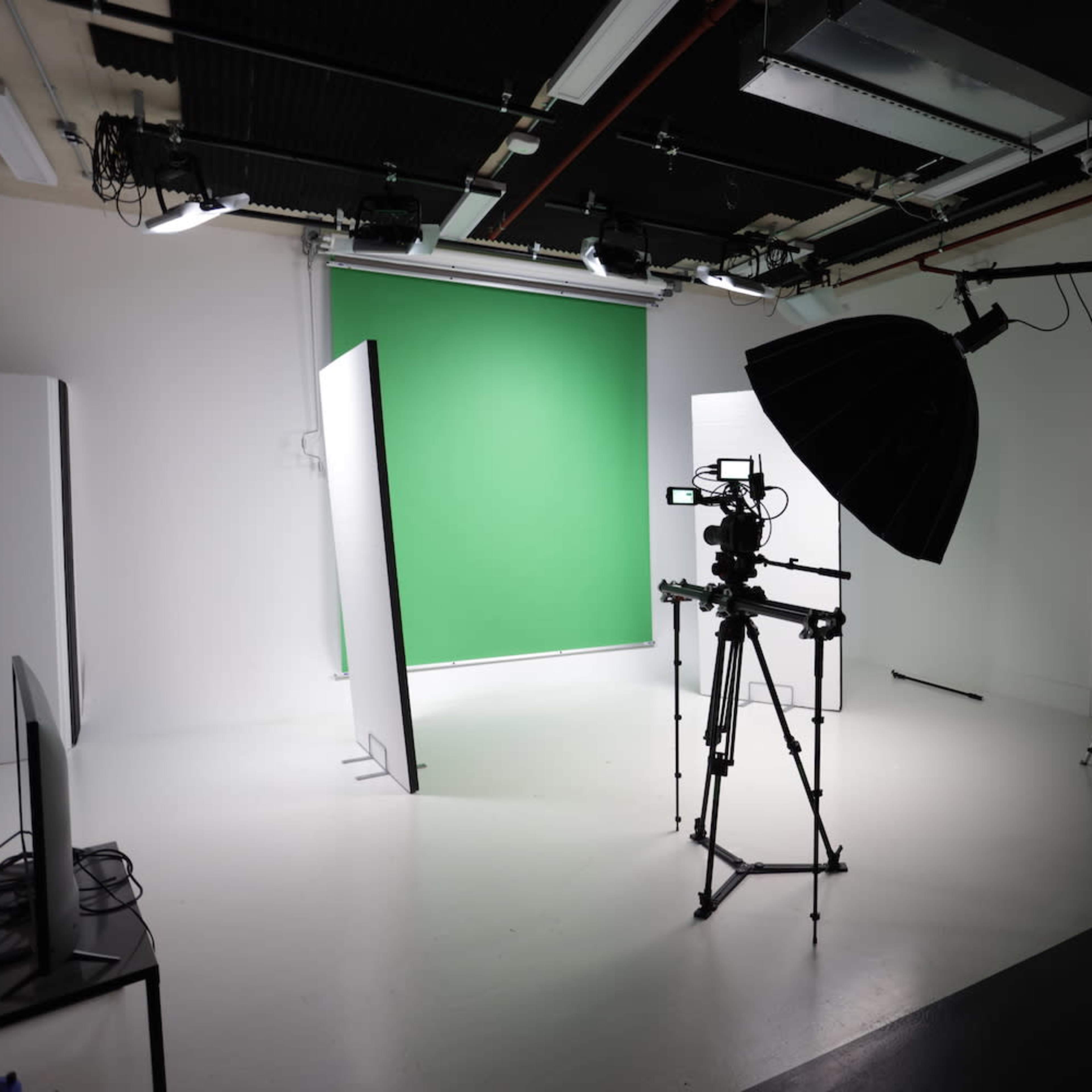 A photography studio is set up with a green screen, lighting equipment, and cameras on tripods.