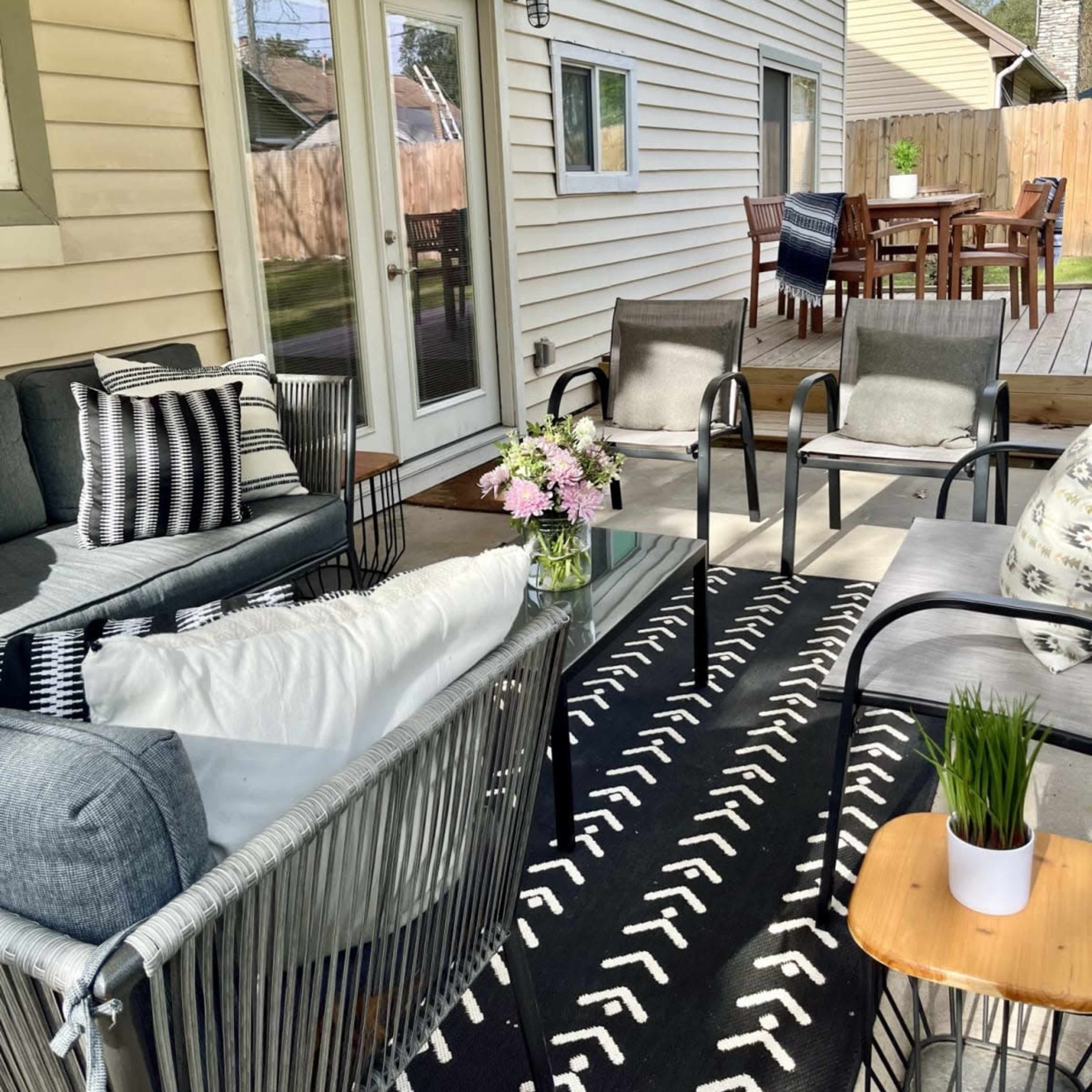 A patio area with a seating arrangement, a coffee table with flowers, and a dining table in the background.
