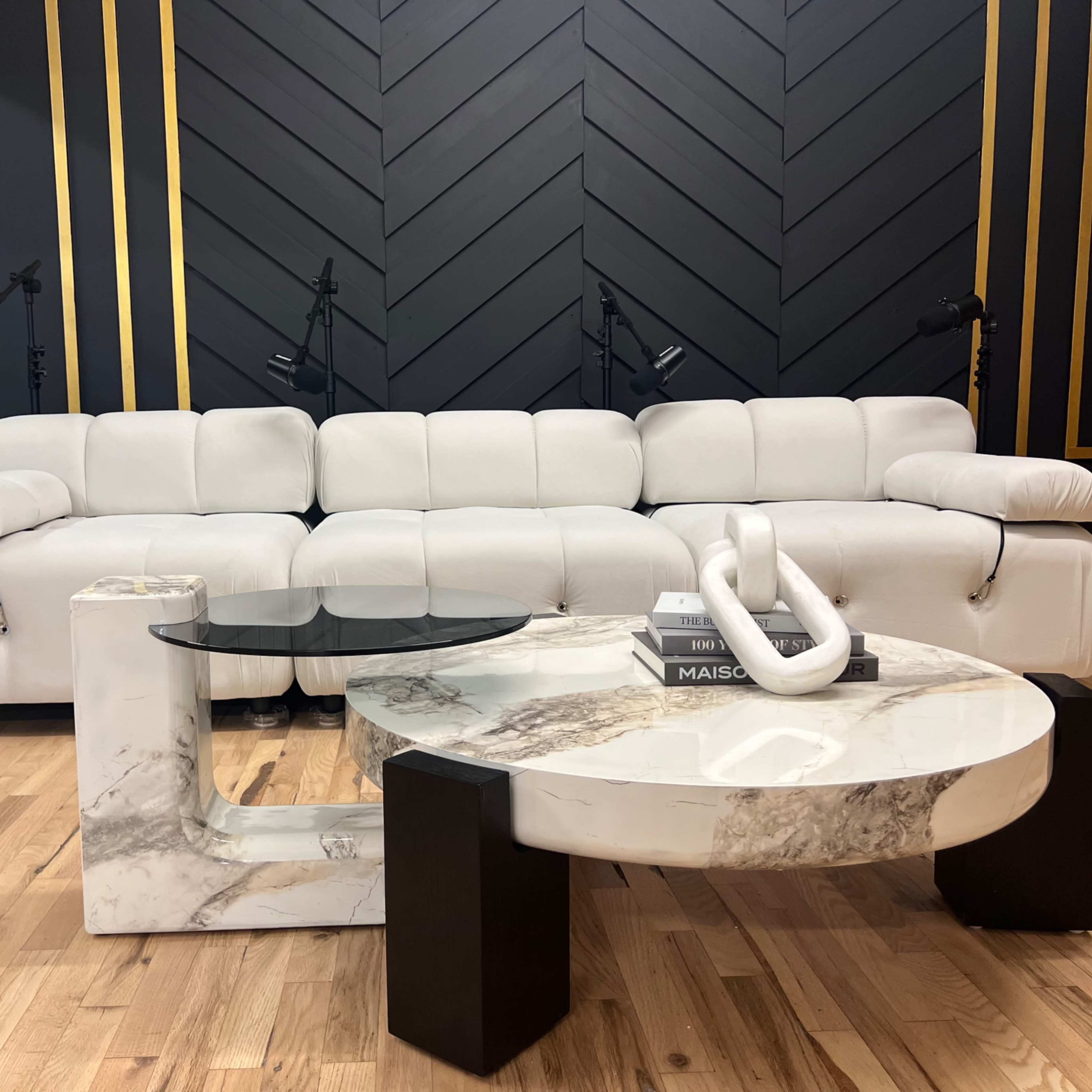 A modern living room setup featuring a white sectional sofa and two distinct coffee tables, one circular and one rectangular, both with marble and black accents.