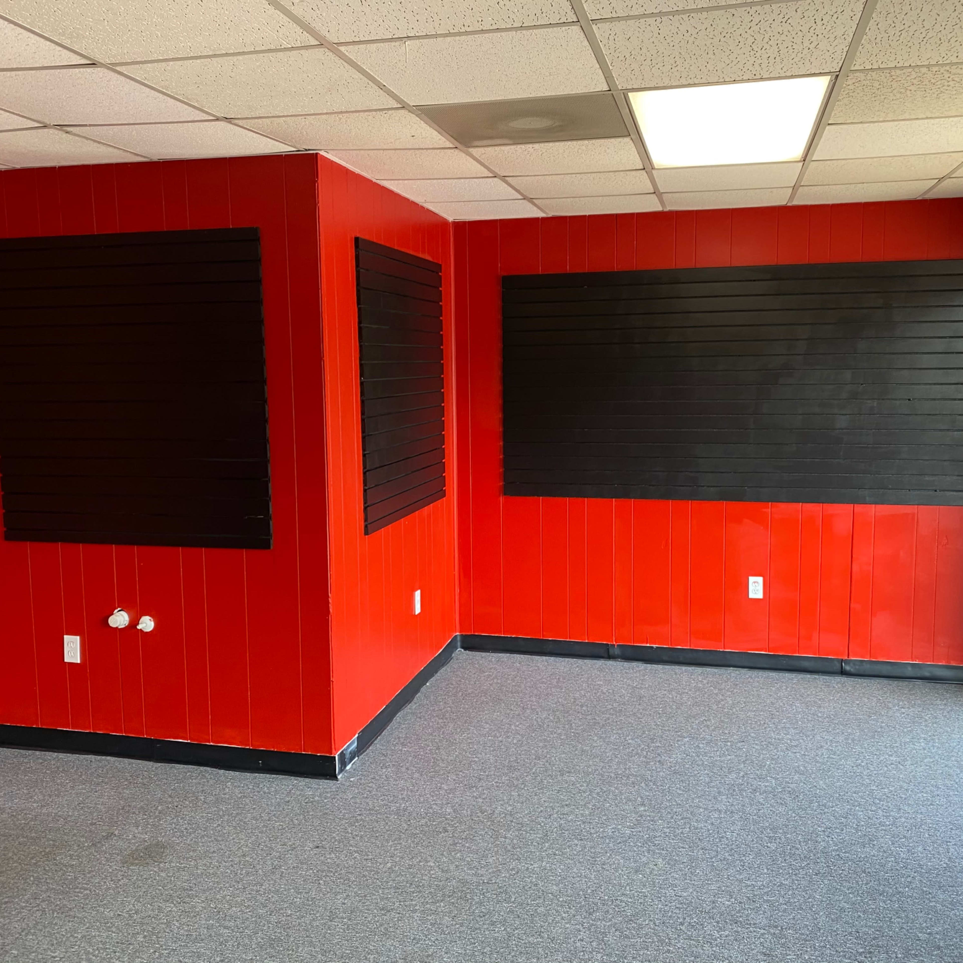 A room with red walls, black wooden wall panels, and gray carpeting.