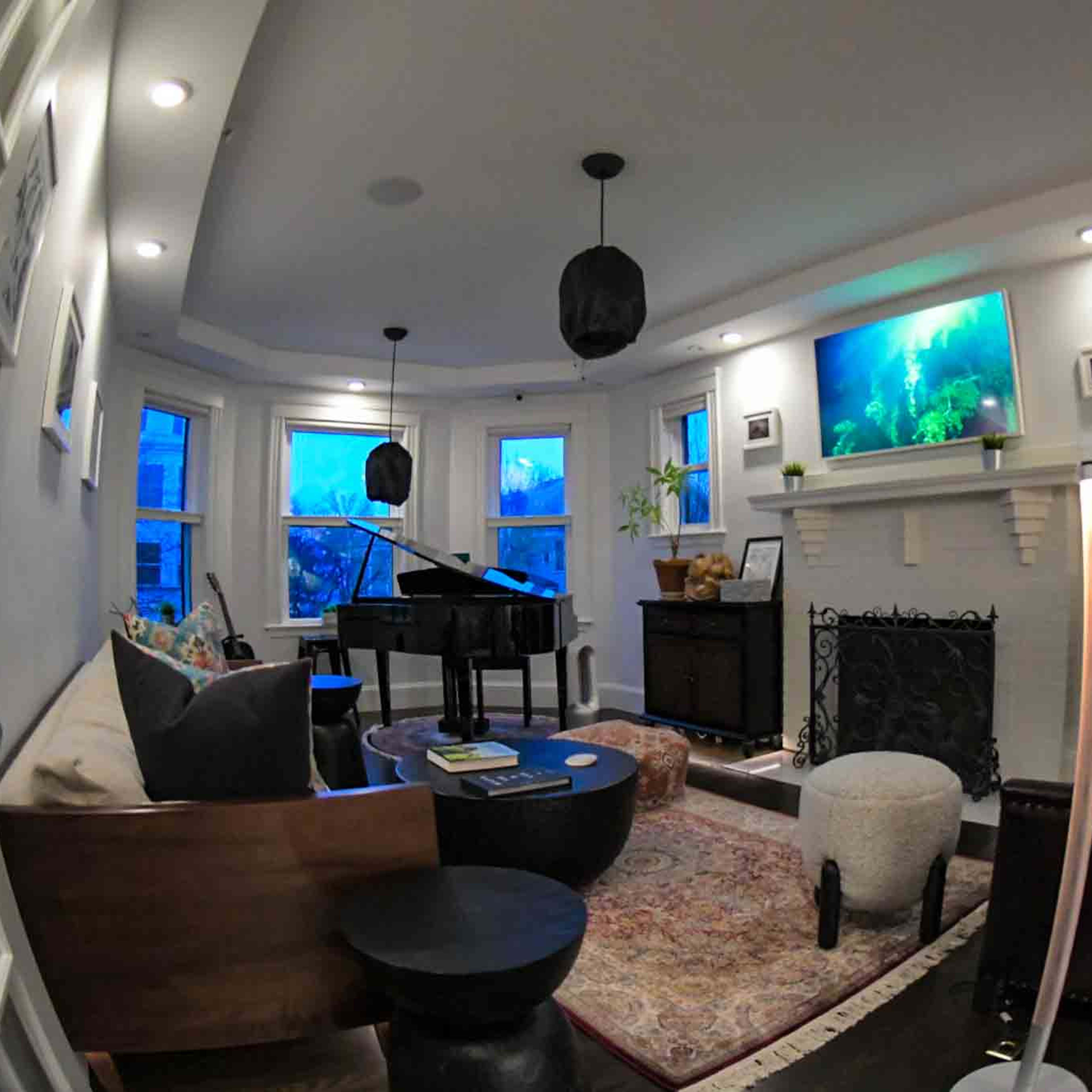 A cozy living room featuring a piano, a fireplace with a television above it, and large windows allowing natural light to enter.