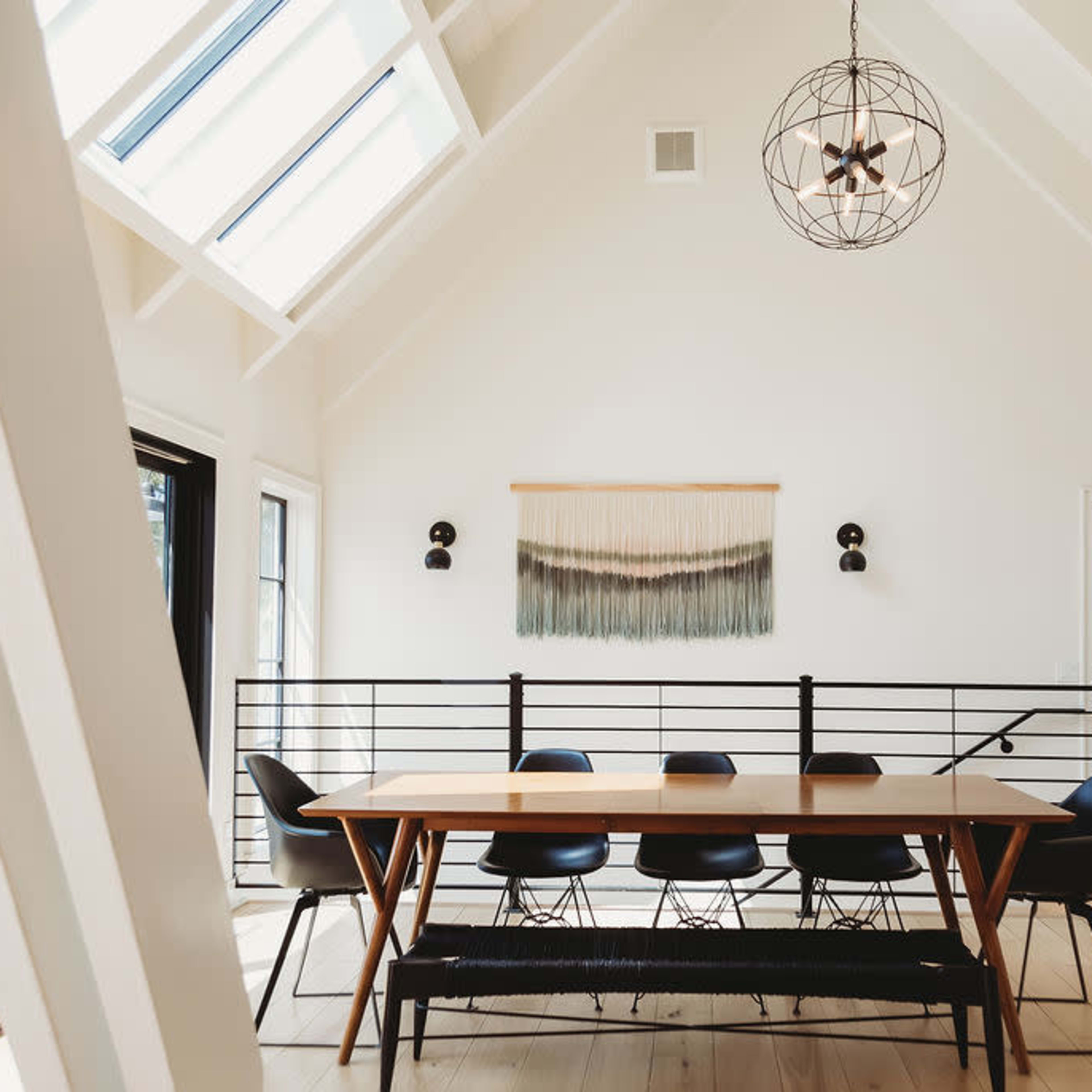 A modern dining area features a long wooden table surrounded by black chairs under a geometric pendant light.