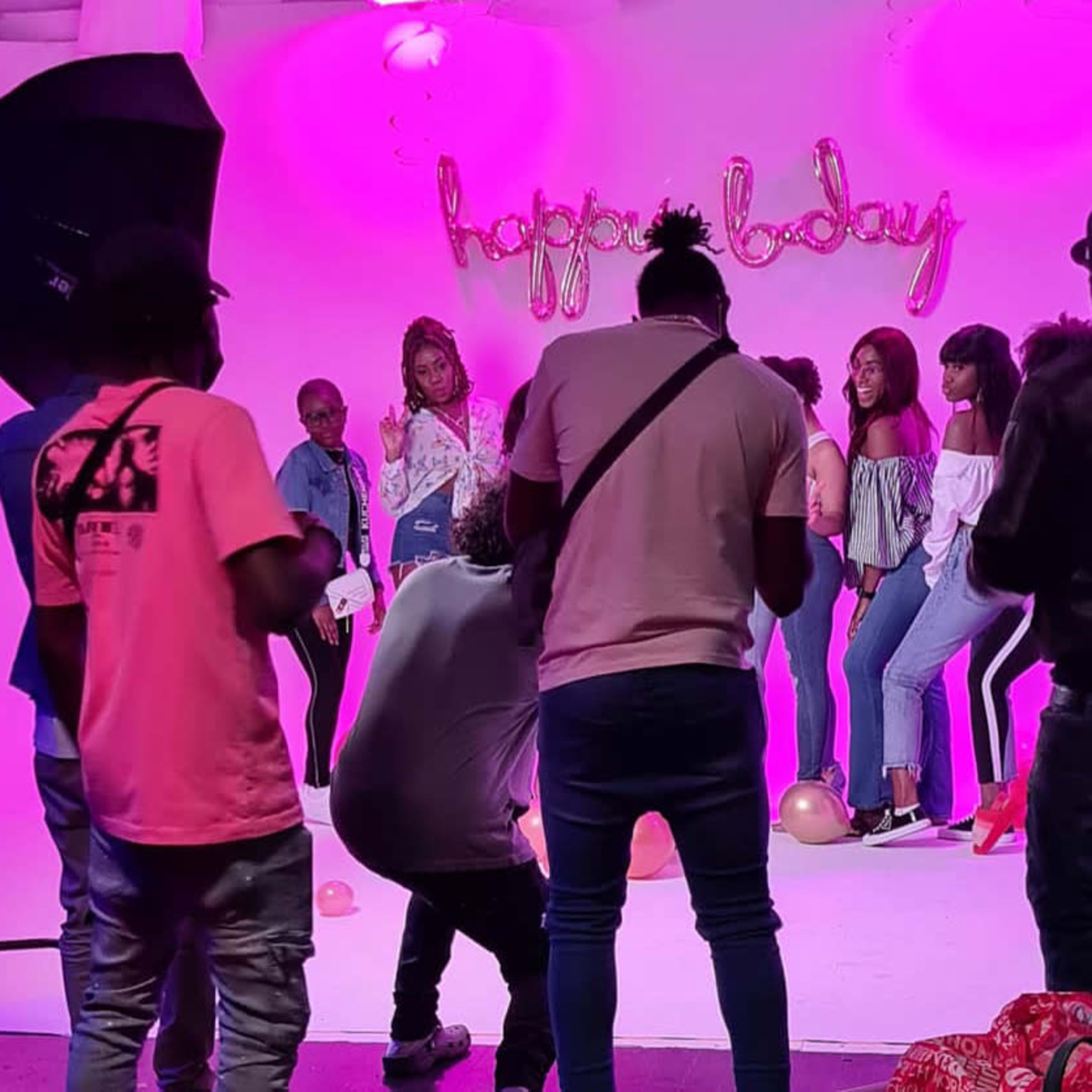 A group of people poses for a photo in front of a backdrop with "happy today" written in pink letters while a photographer captures the scene.
