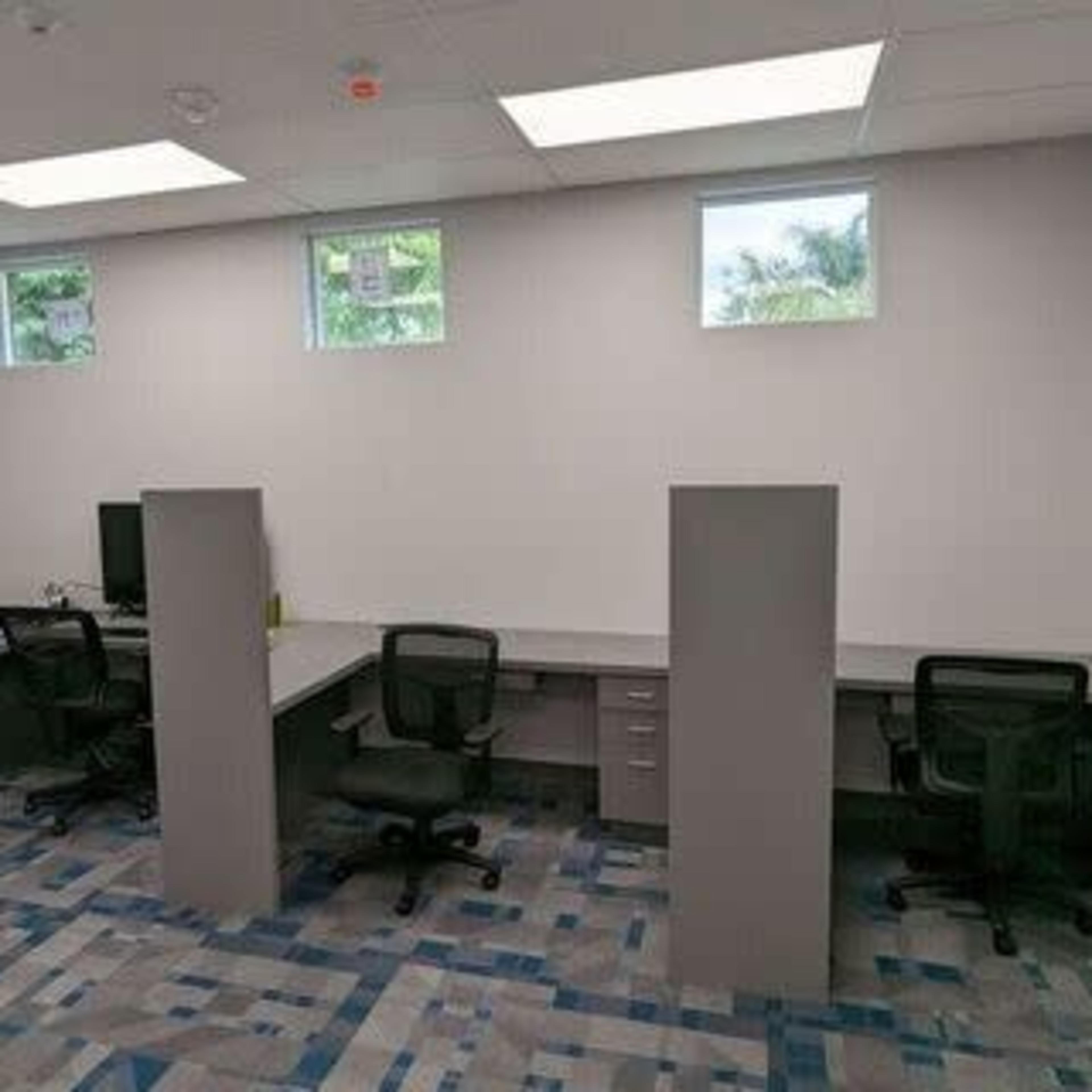 A modern office space with four desks separated by gray dividers, two chairs per desk, and a computer setup in one corner.