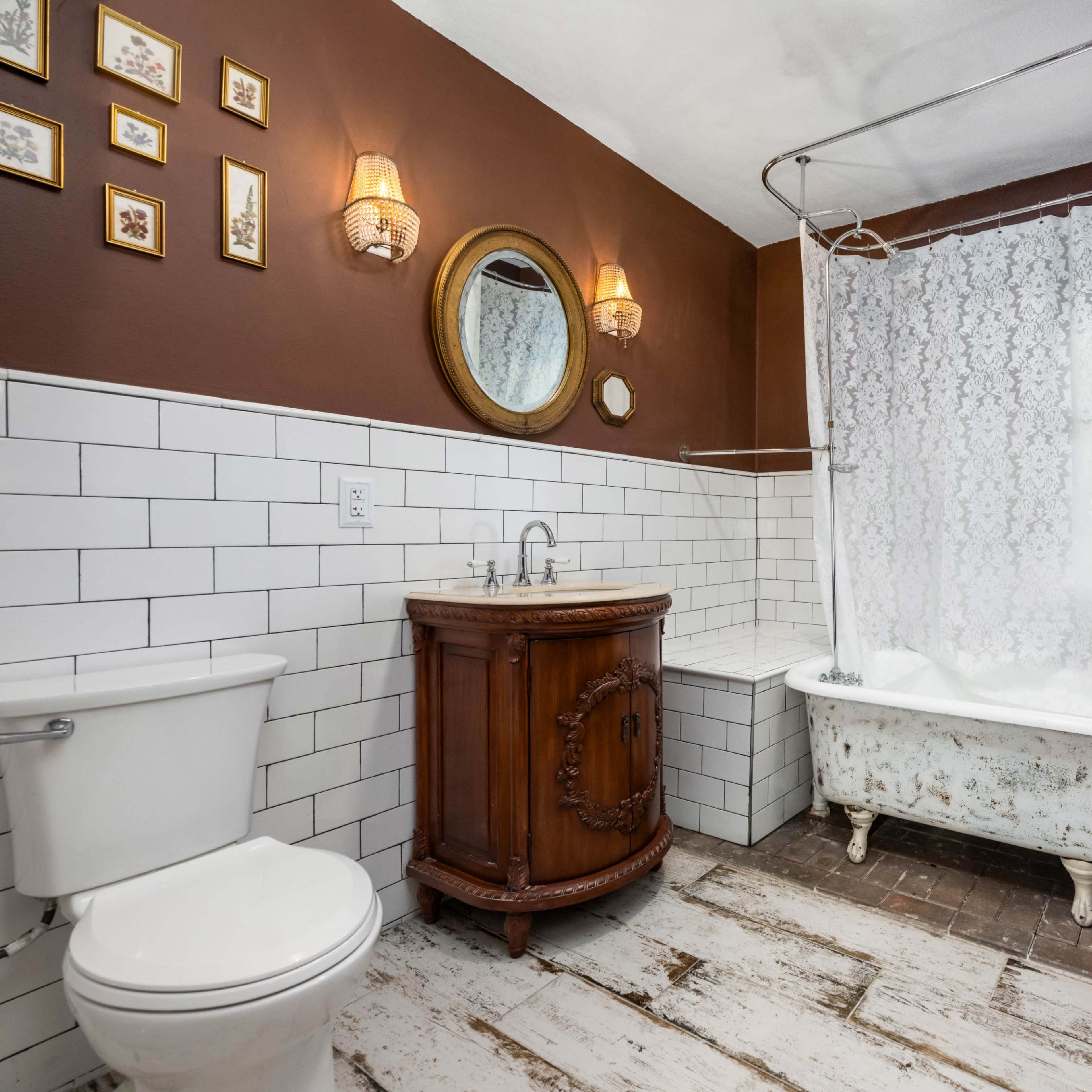 A vintage bathroom featuring a clawfoot bathtub, a round mirror, a wooden vanity, and white tiled walls.