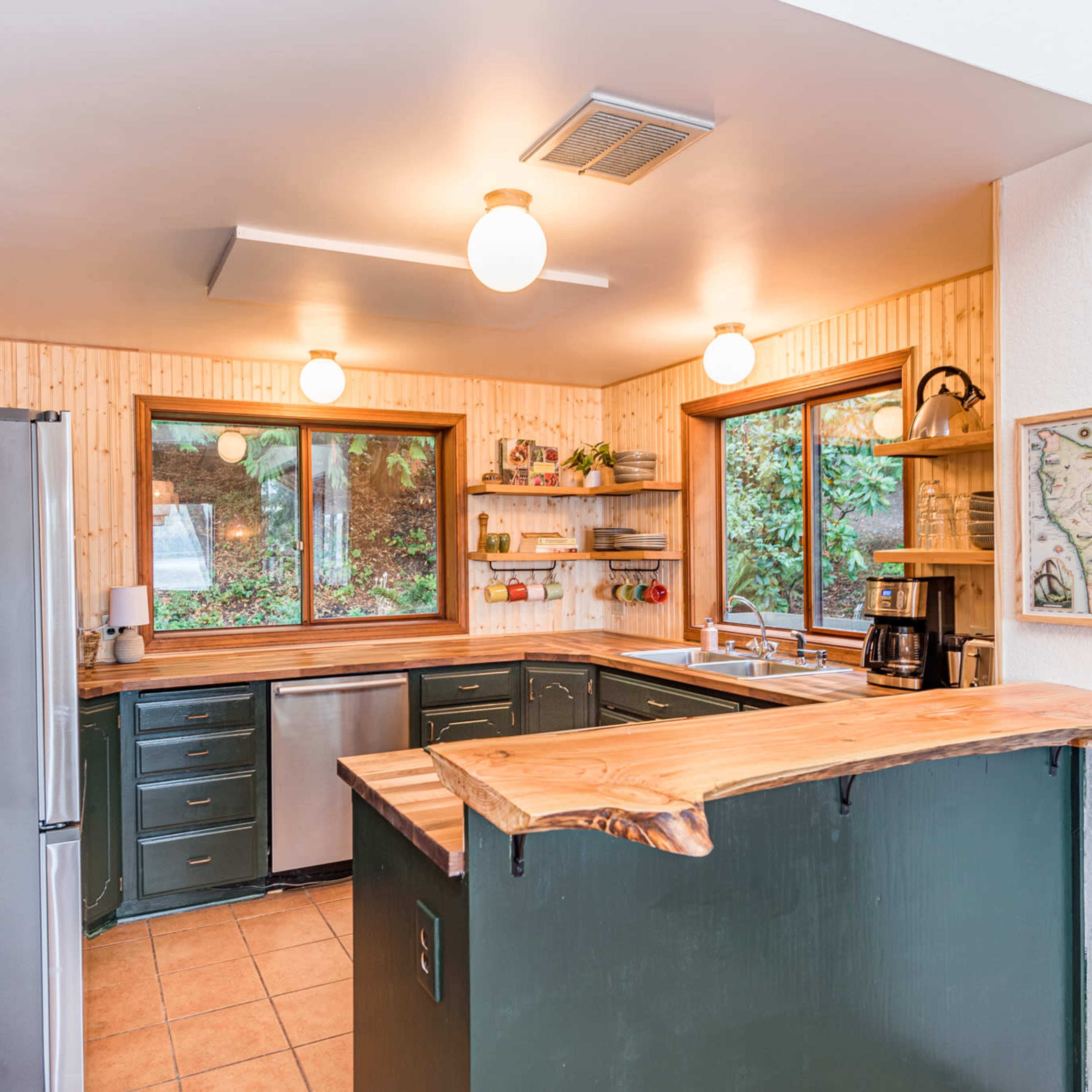 The kitchen features green cabinetry, wooden countertops, and large windows offering views of the outdoors.