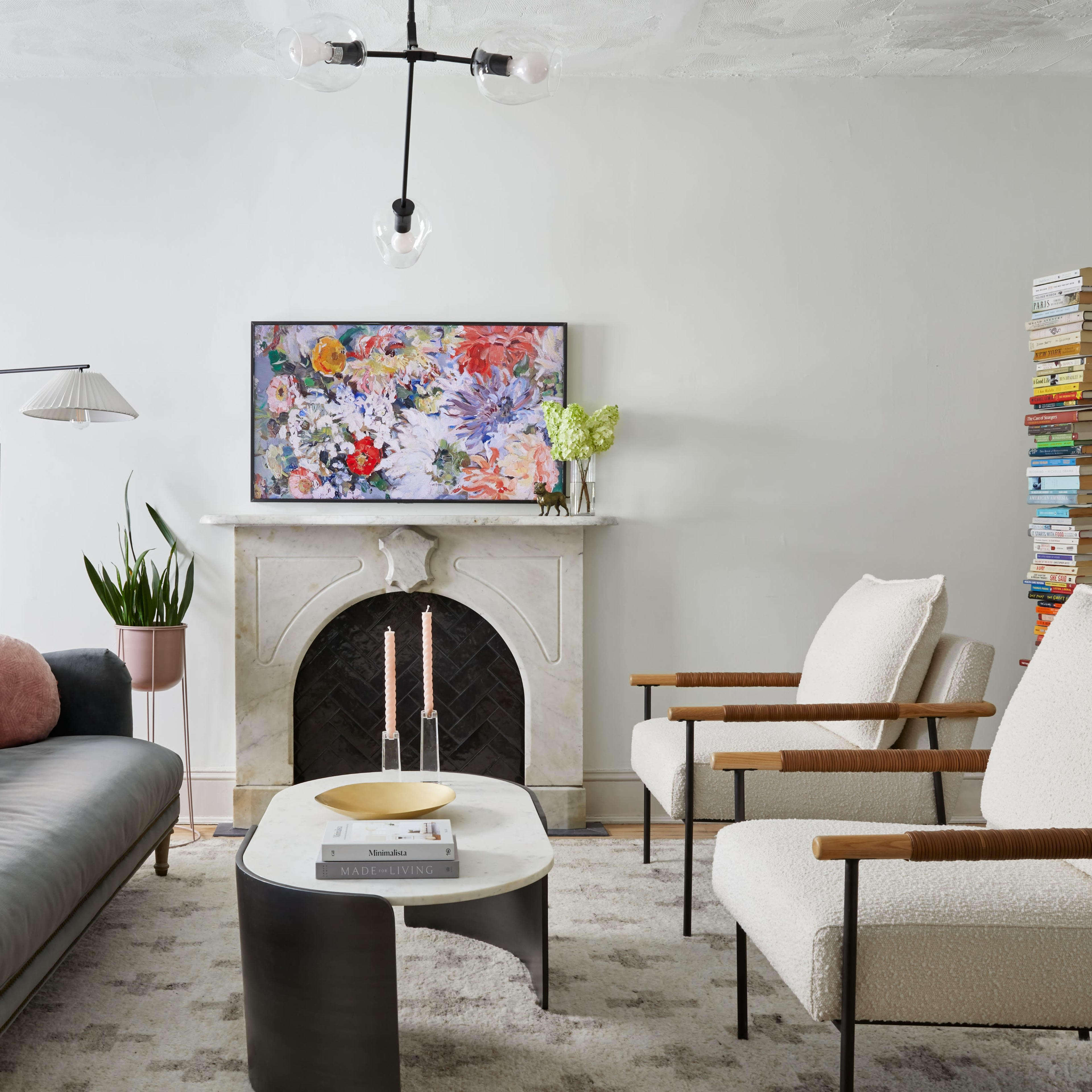 A modern living room with a sofa, two armchairs, a coffee table, and a decorative fireplace, featuring a floral artwork above it.