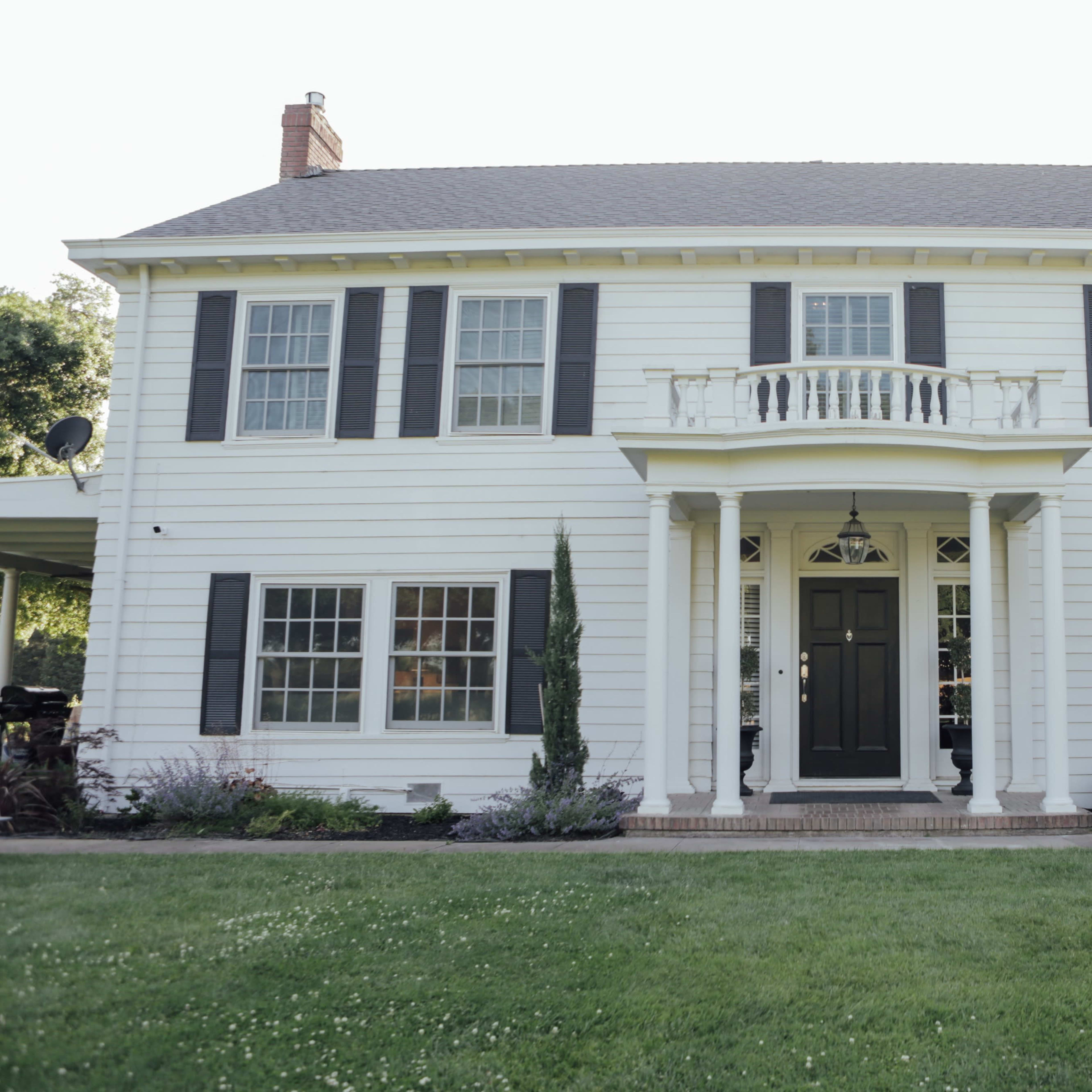 A large, two-story white house with black shutters and a decorative balcony above the front door.