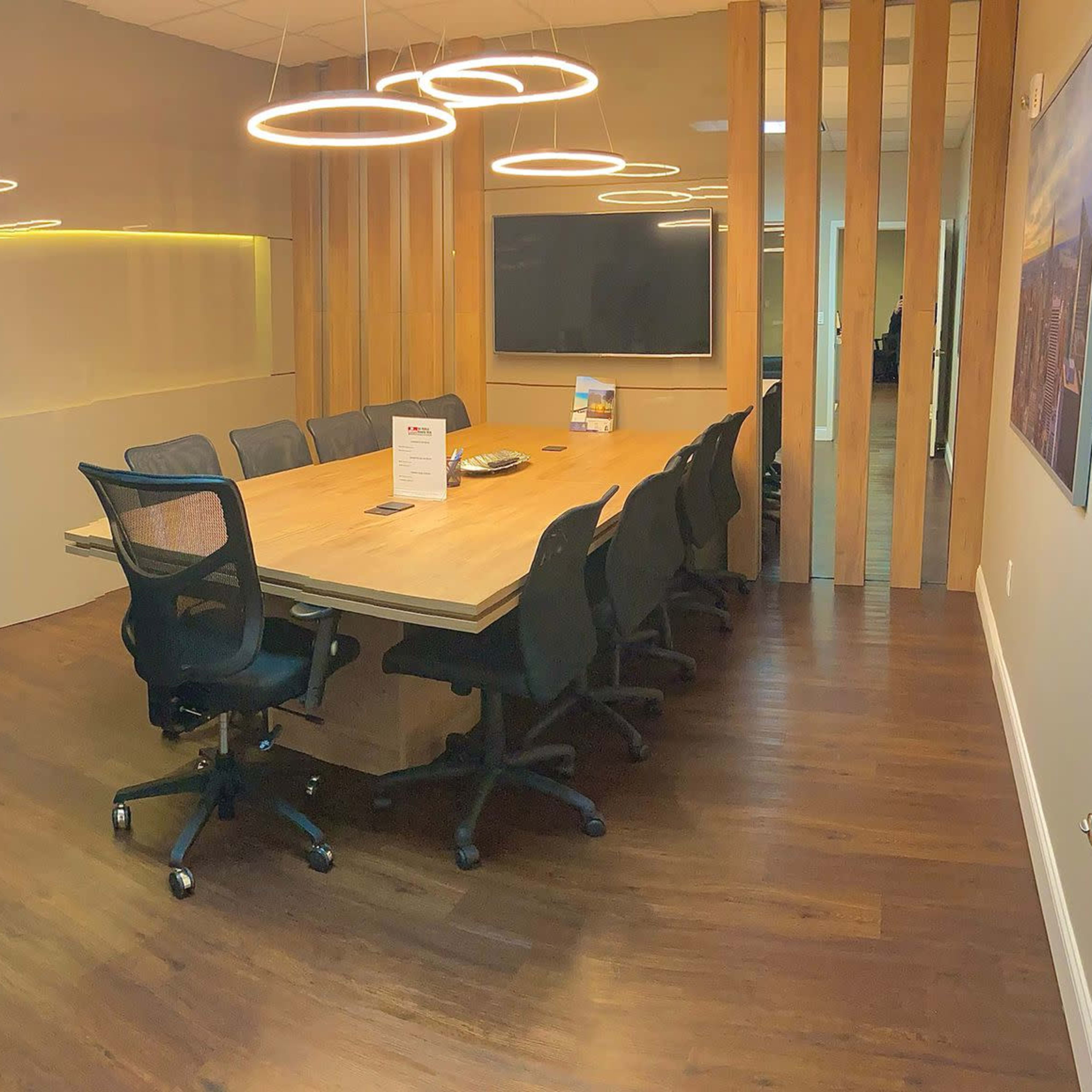 A modern conference room features a large wooden table surrounded by black office chairs, with a coffee station and a sleek cabinet along one wall.