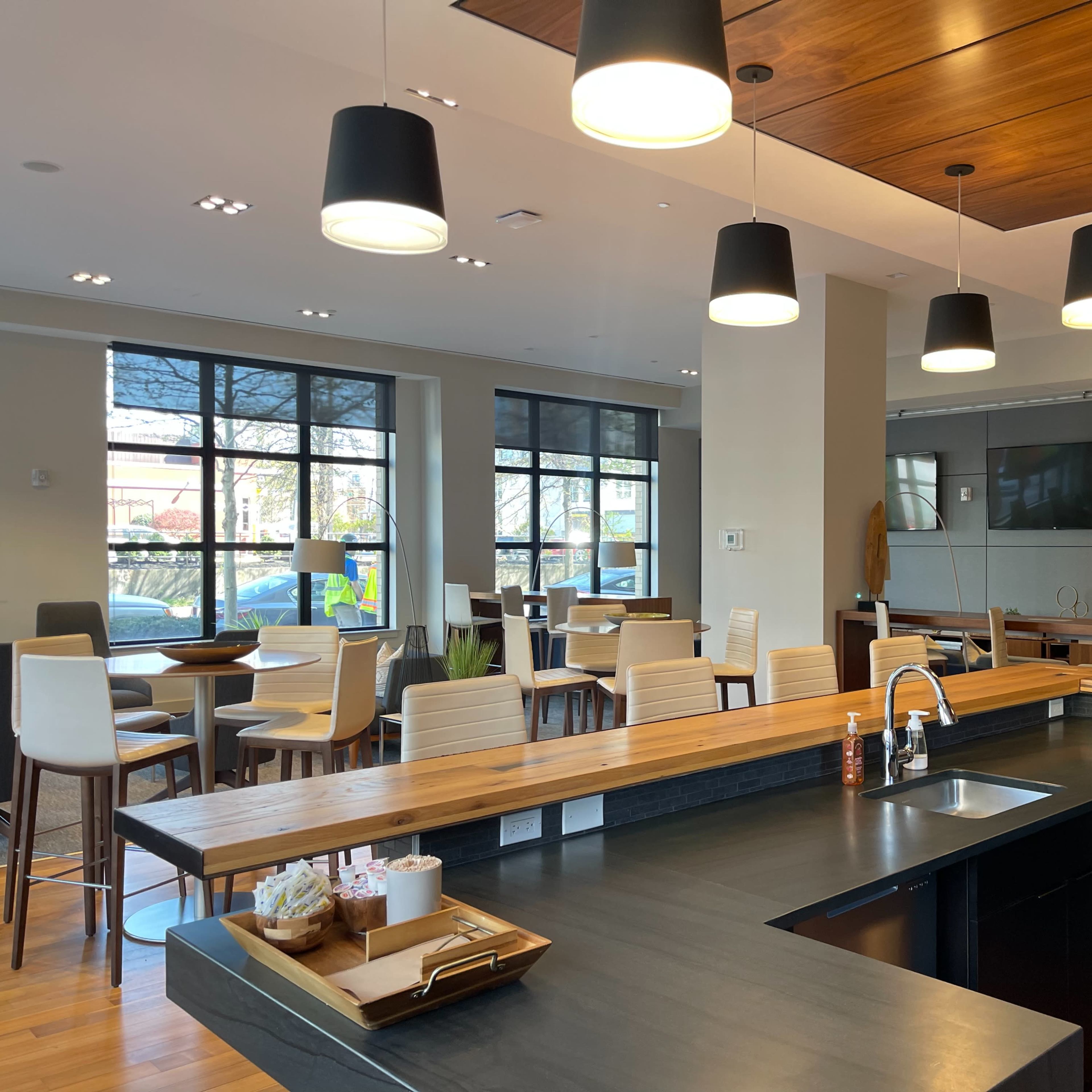 A modern café interior featuring a wooden counter, high-top tables, and pendant lighting.