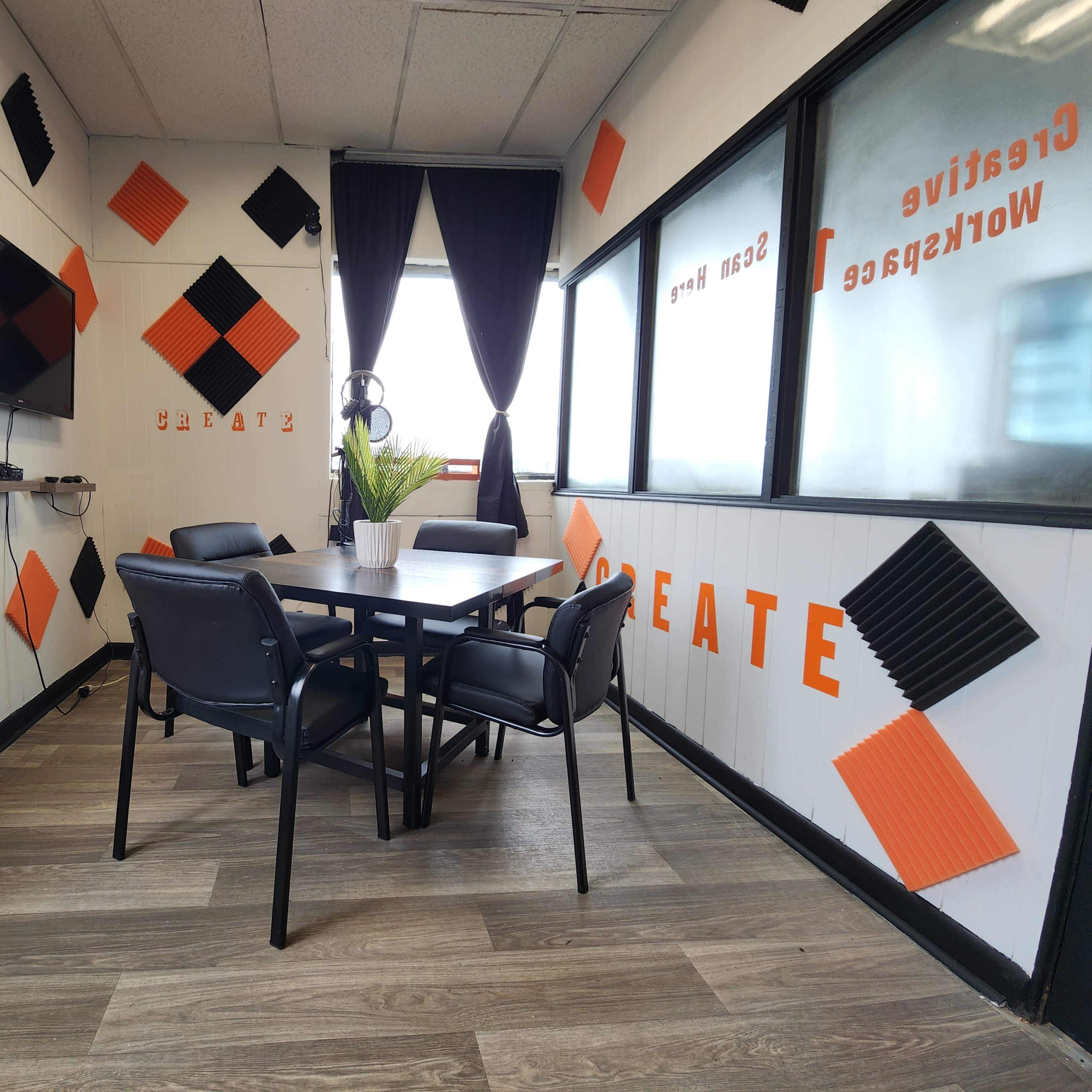 A small meeting room with a table surrounded by chairs, decorated with orange and black geometric shapes on the walls, and a large television mounted on one side.
