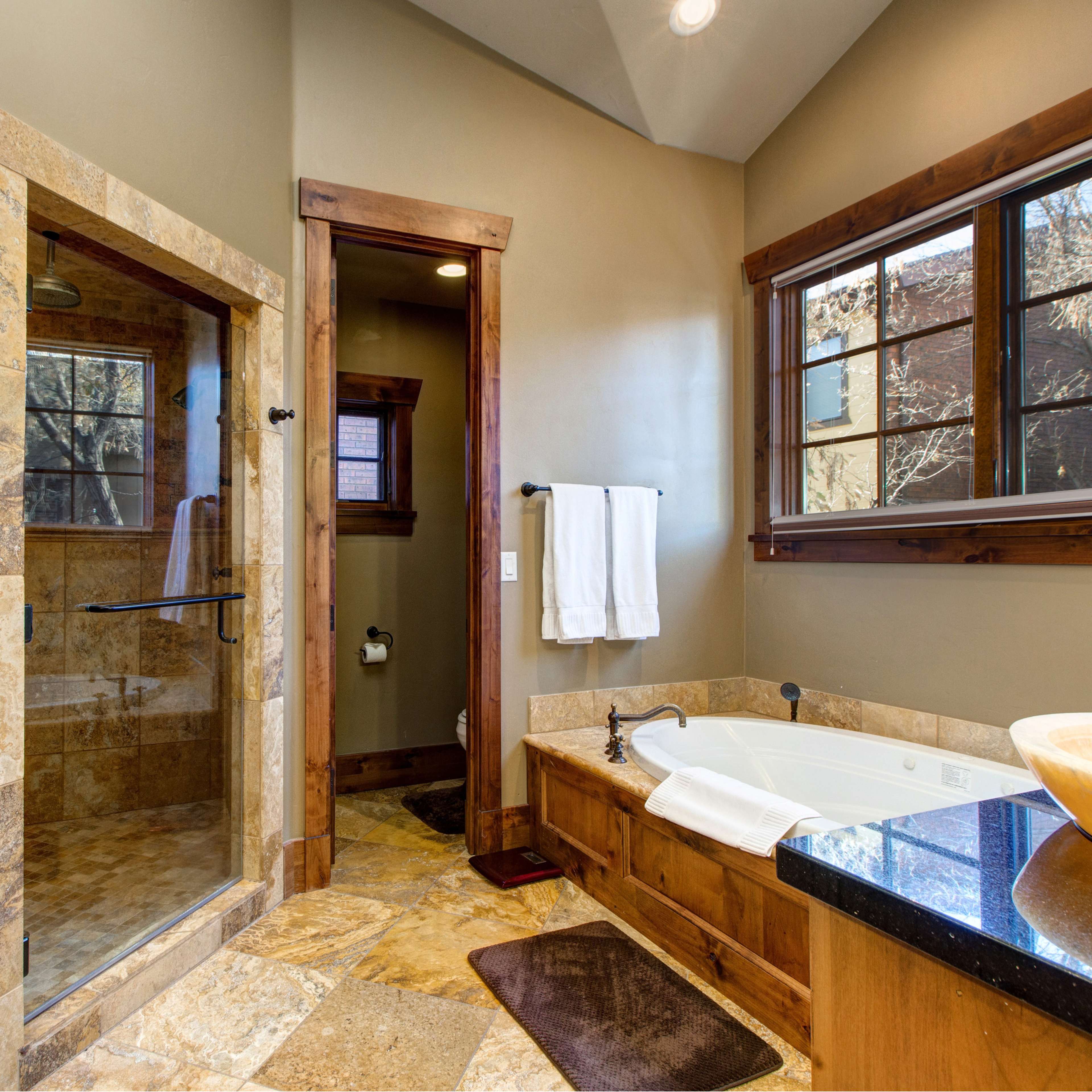 A well-designed bathroom featuring a glass-enclosed shower, a freestanding bathtub, double sinks with bowl-style basins, and stone tile flooring.