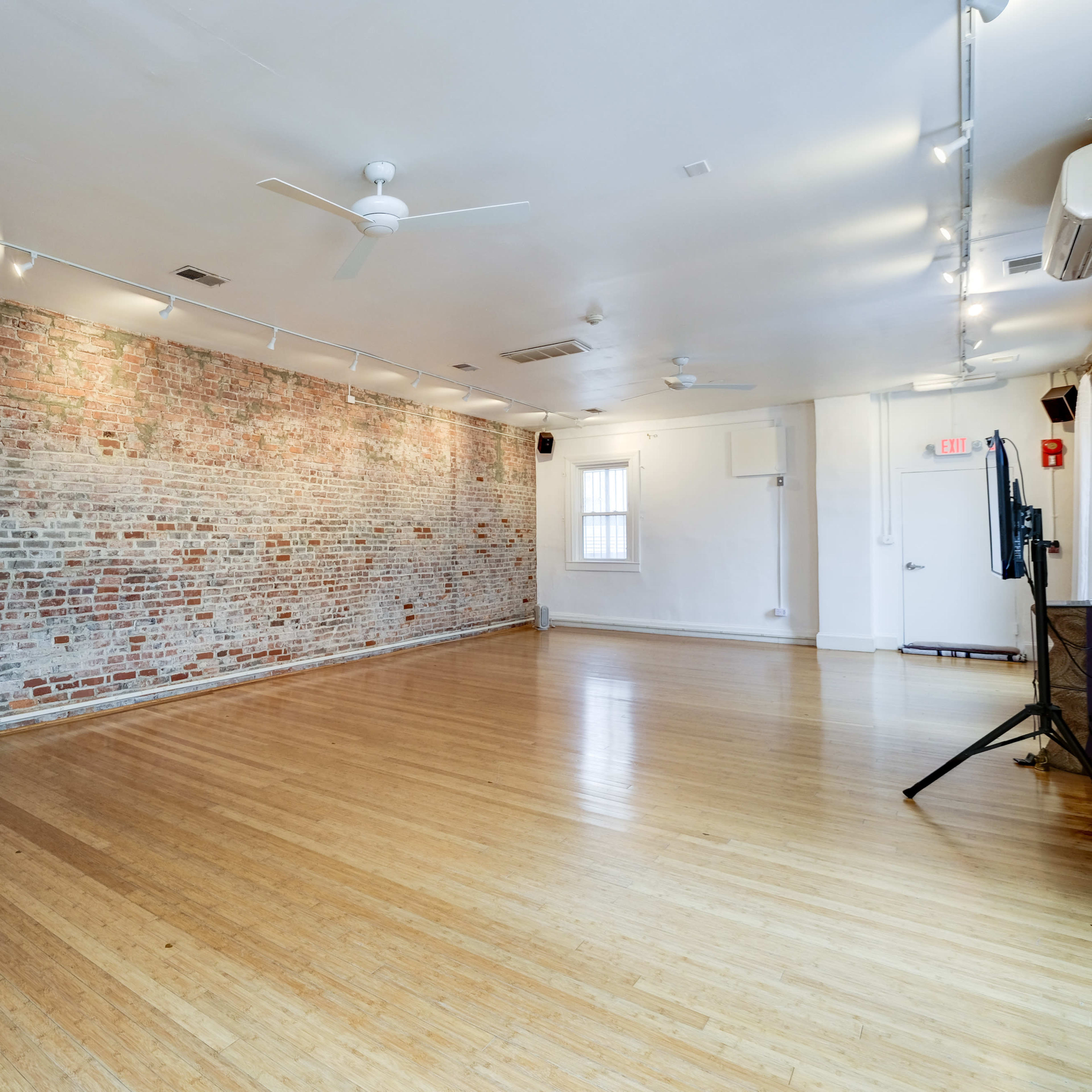 An empty room with hardwood flooring and a brick wall, illuminated by ceiling lights.