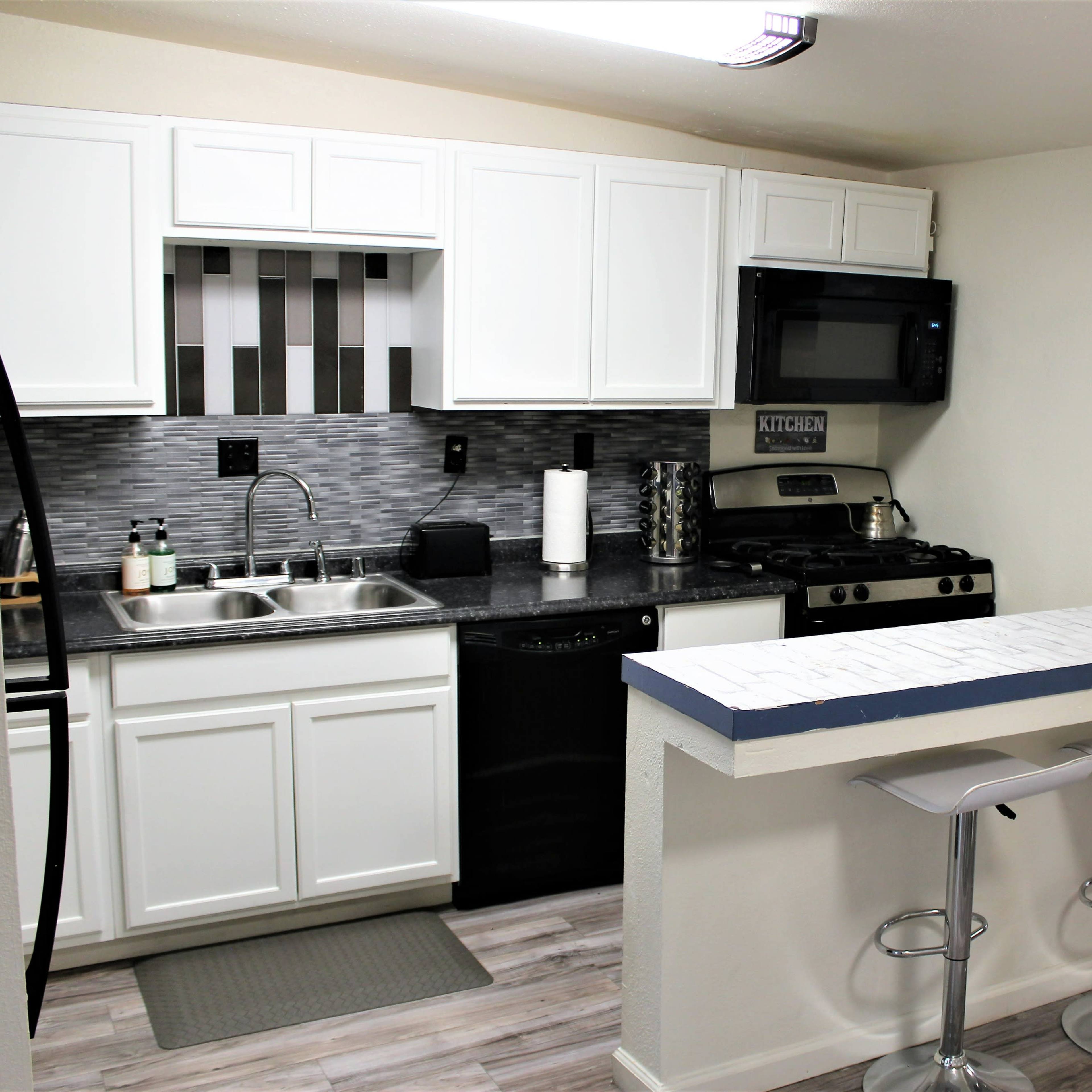 A modern kitchen with white cabinets, a black countertop, and bar seating with two stools.