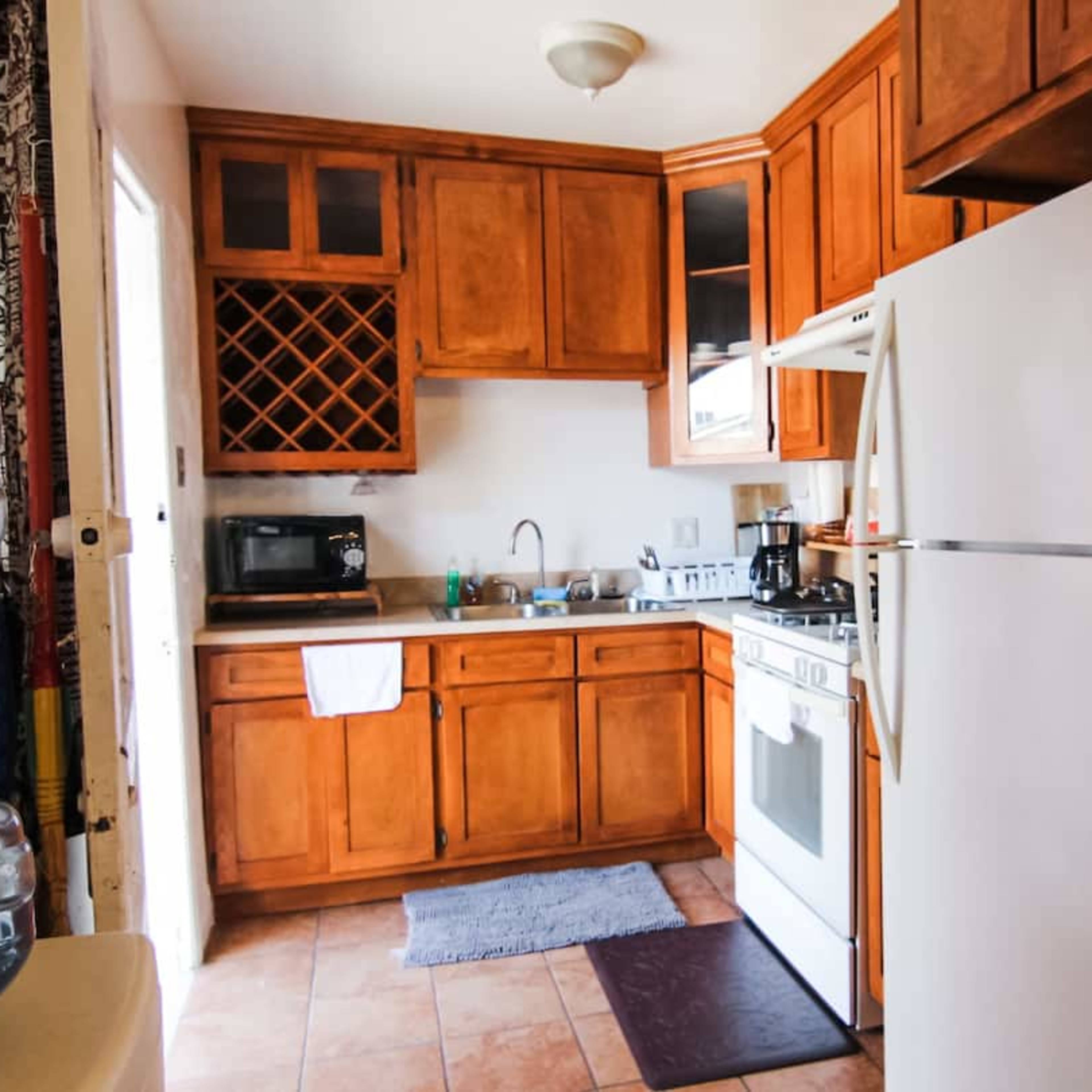 A compact kitchen with wooden cabinets, a white refrigerator, and a stove, featuring a water cooler and a small dining area.