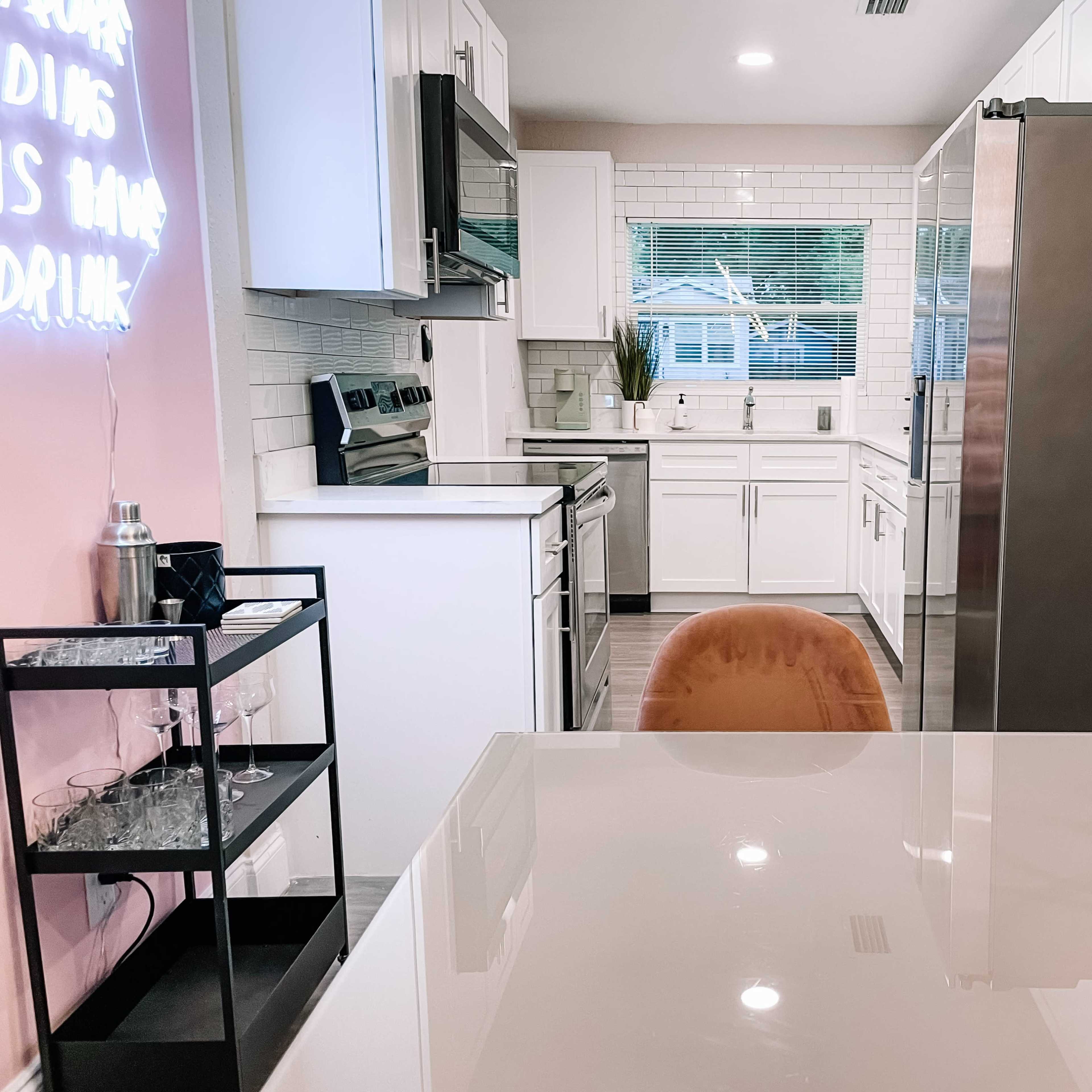 A modern kitchen with white cabinets, stainless steel appliances, and a grey countertop, featuring a dining area with two chairs and a decorative vase.