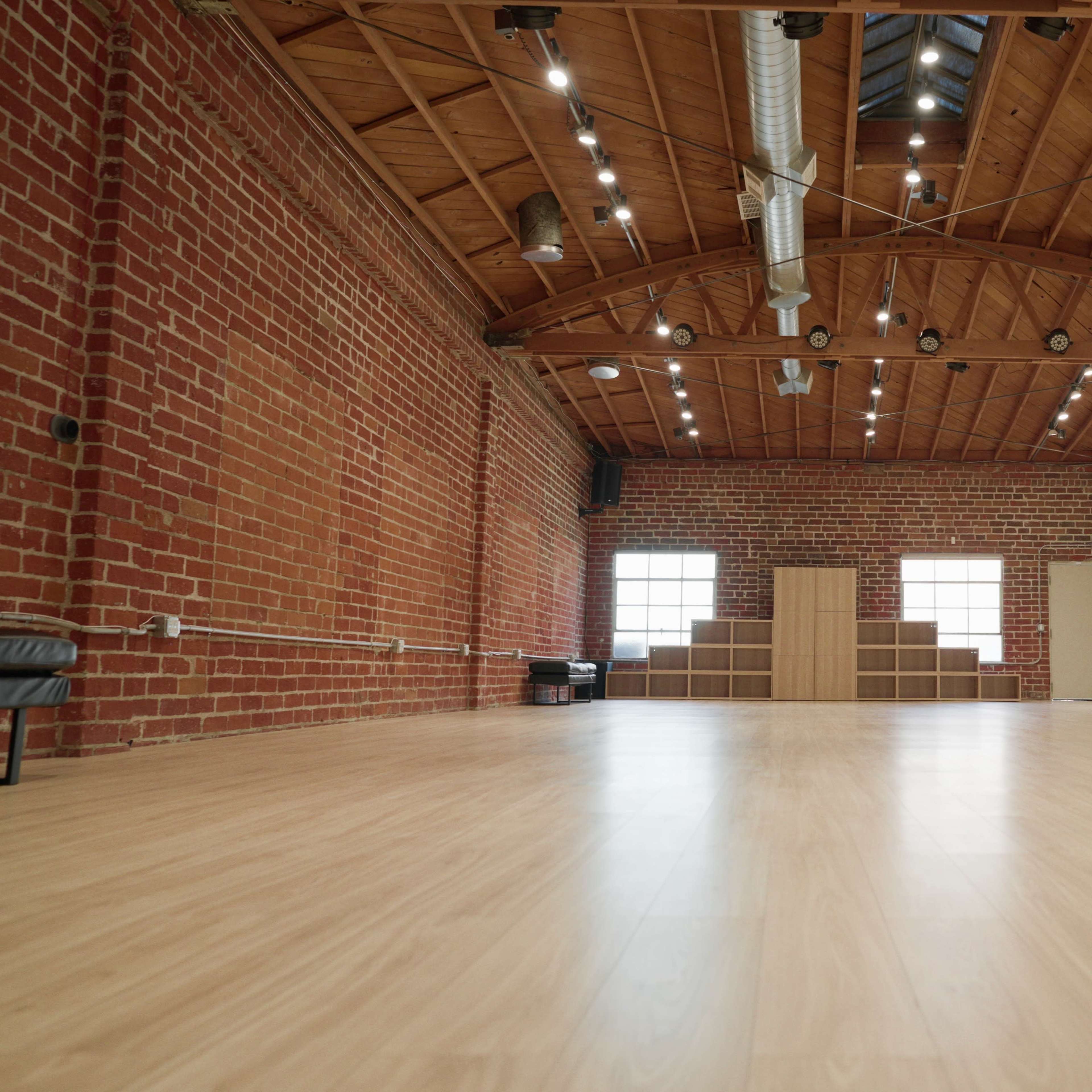 A spacious studio with wooden floors, exposed brick walls, and large windows.