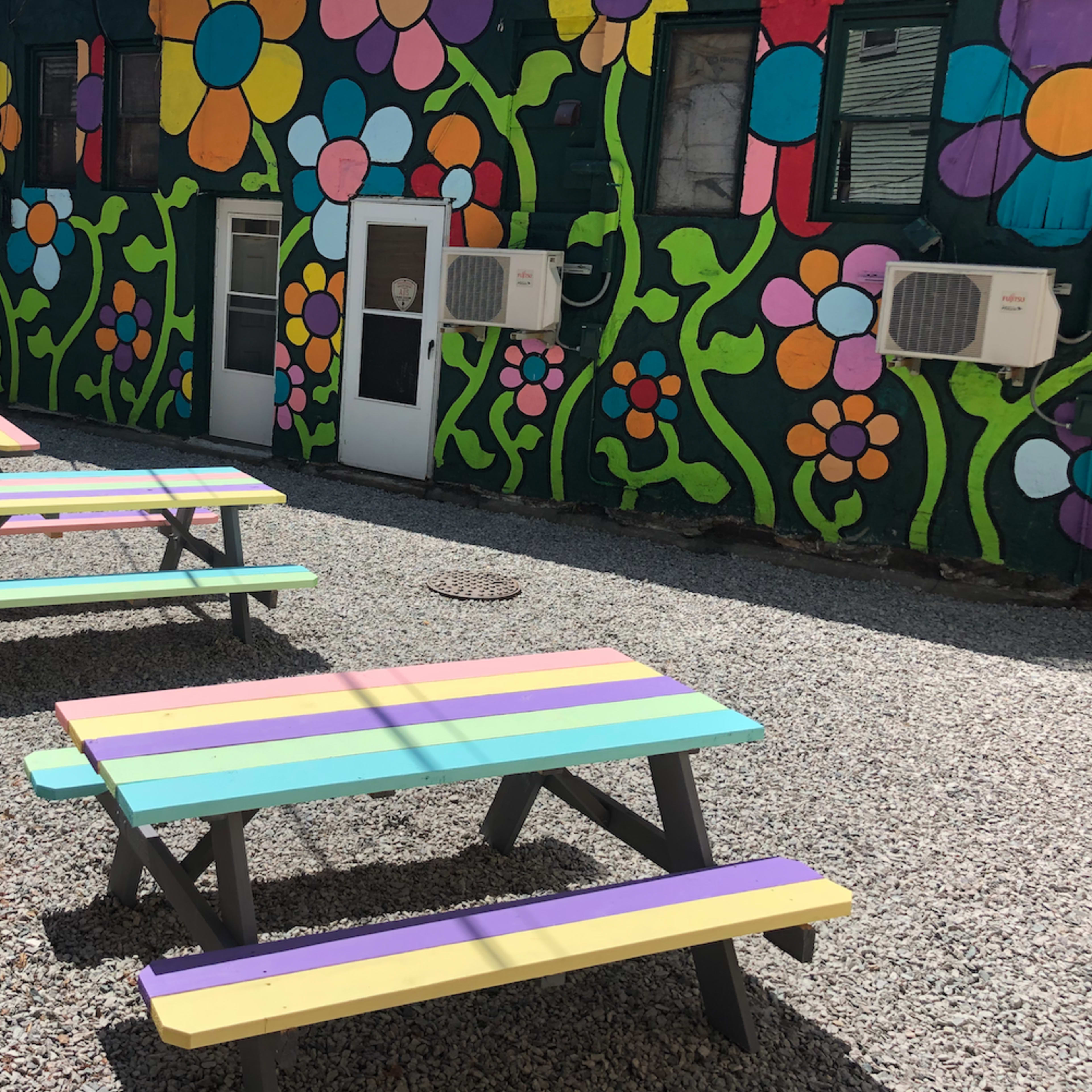 A colorful outdoor area with picnic tables and a vibrant floral mural on the wall.