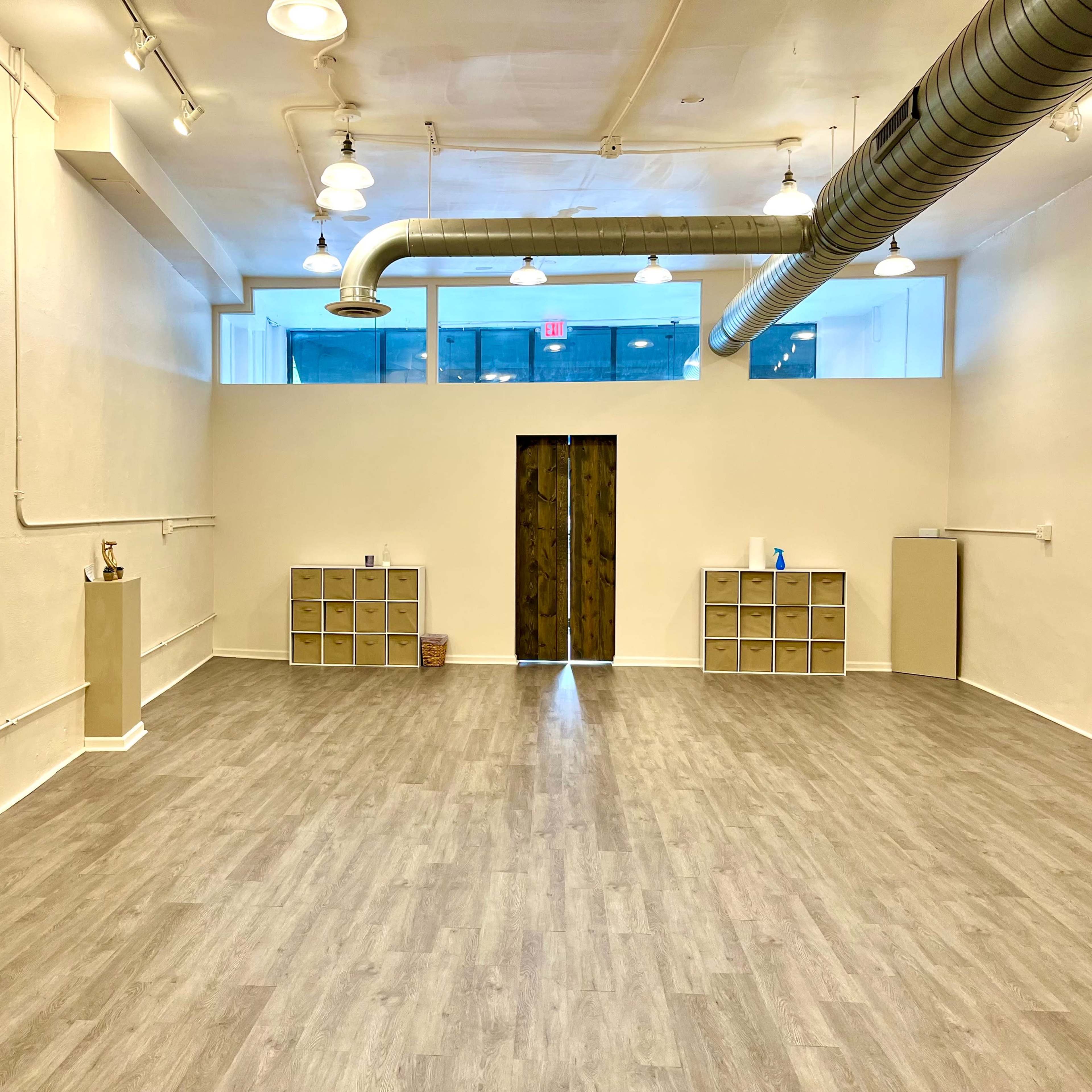 A spacious, brightly lit interior room with wooden flooring, featuring two cabinets on opposite walls, and a wooden door at the far end.