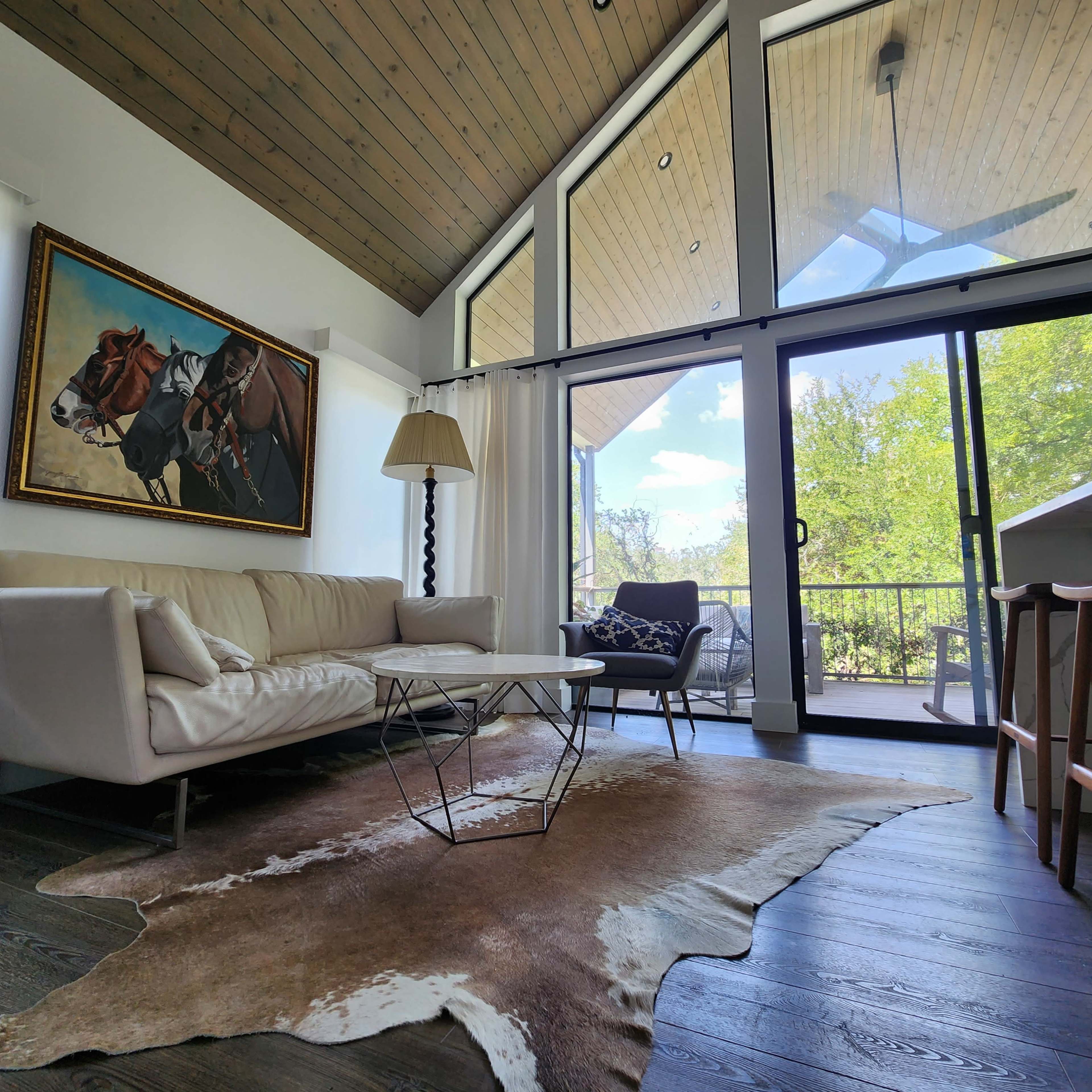 A modern living room with a white sofa, a coffee table, and large windows overlooking a green landscape.
