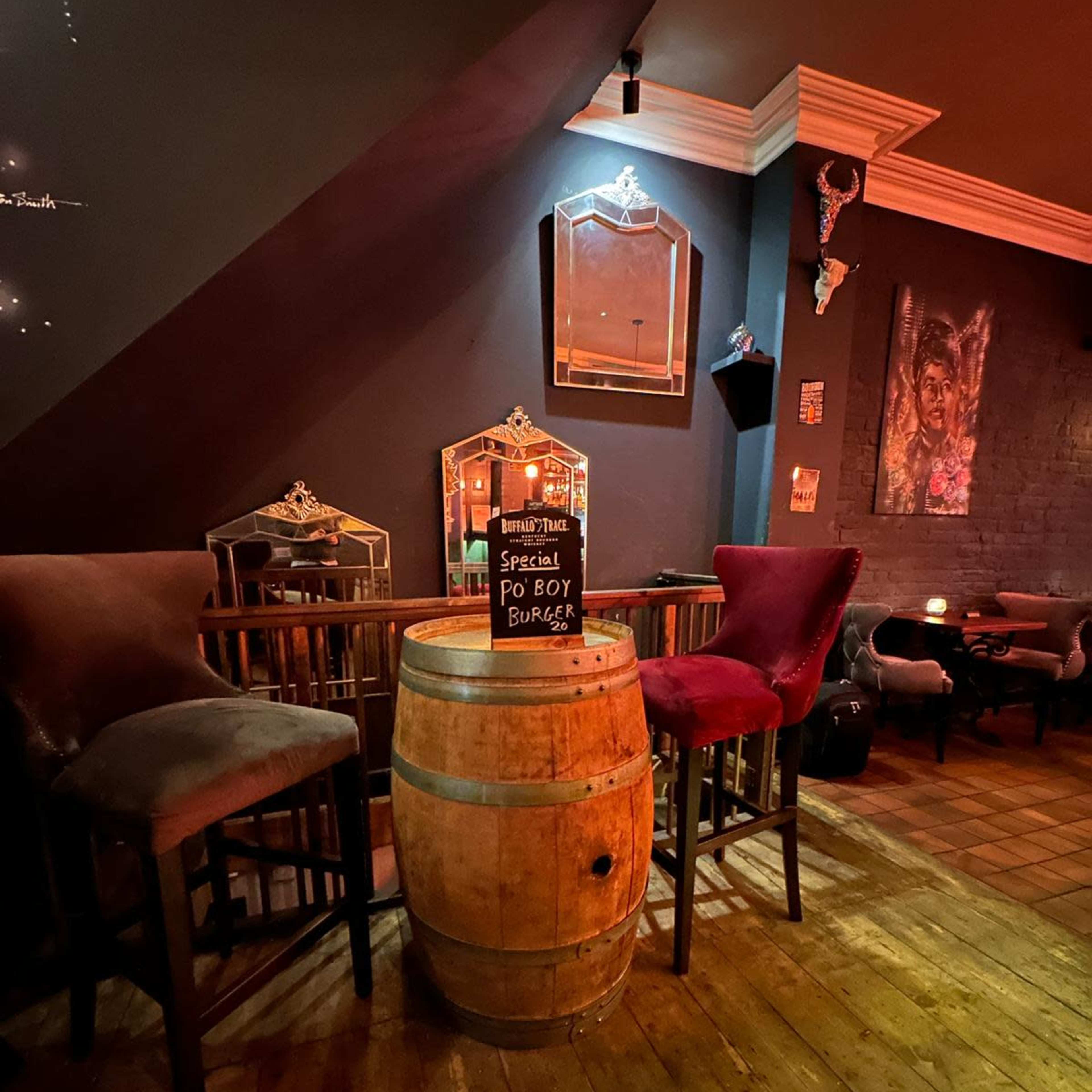 A wooden barrel serves as a table in a dimly lit room with two chairs and a chalkboard sign promoting a special burger.