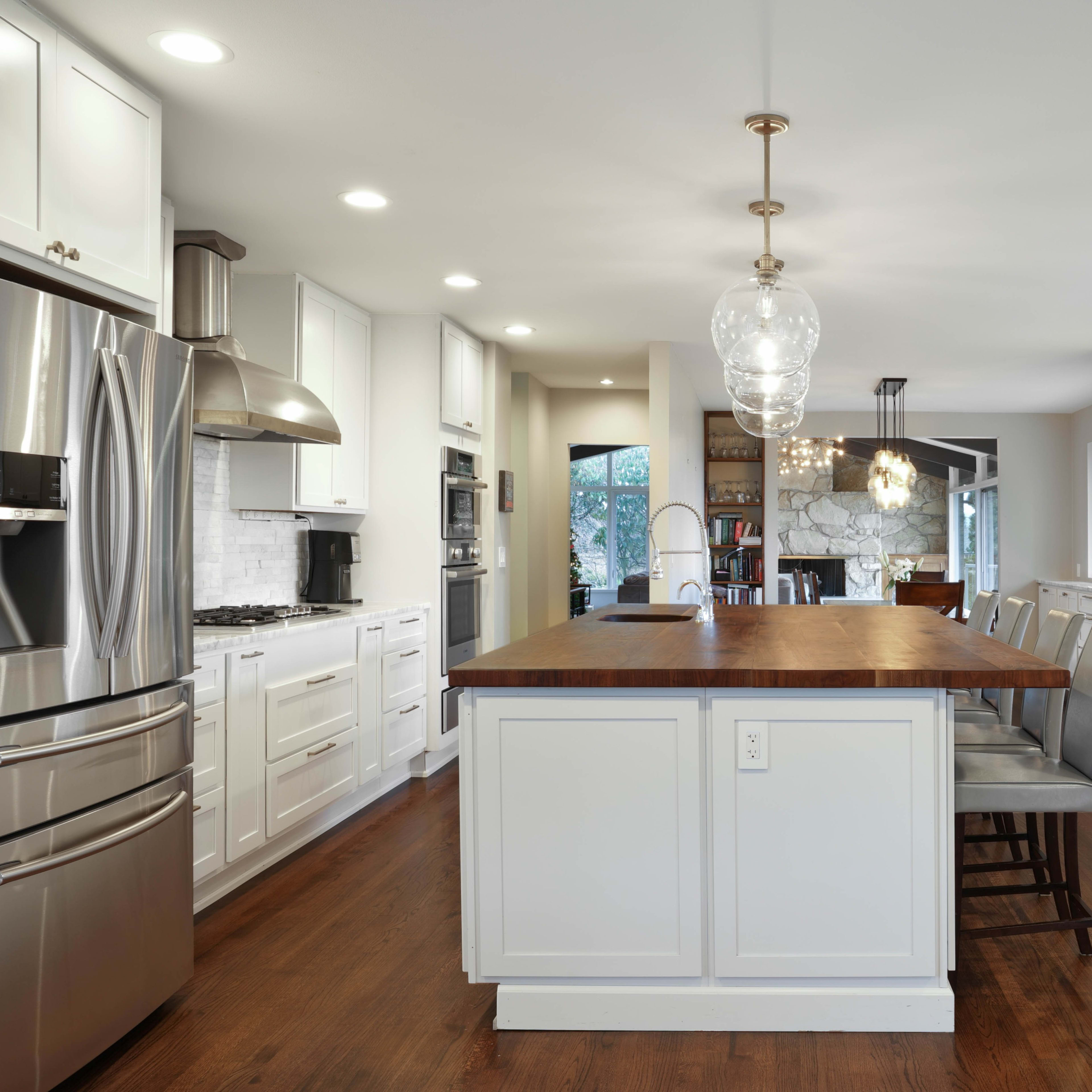 A modern kitchen with white cabinetry, stainless steel appliances, and a central island featuring a wooden countertop and bar seating.