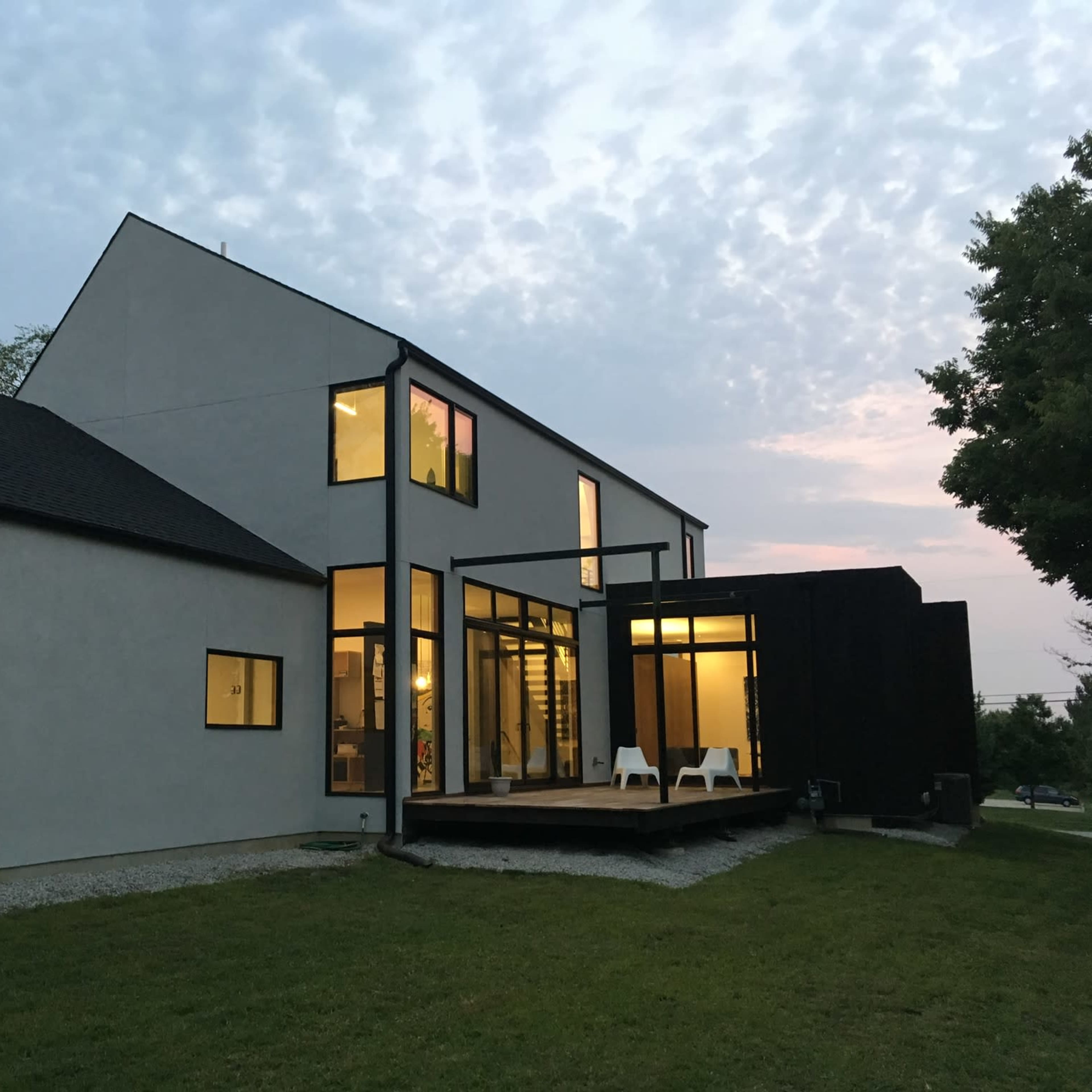 A modern house features a mix of textured walls and large windows, with a wooden deck and lawn in the foreground.