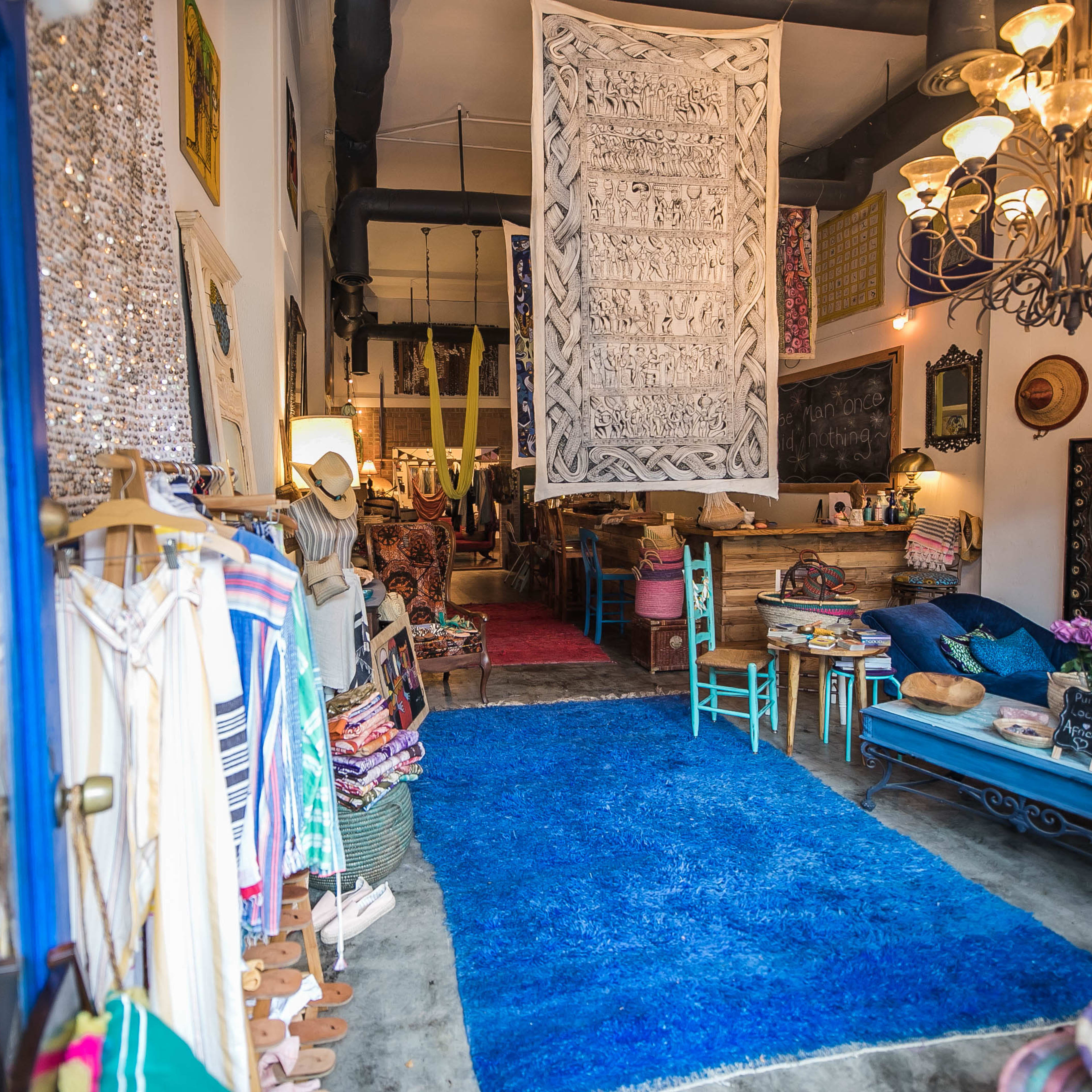 A boutique interior with colorful textiles, a large blue rug, and various decorative items displayed throughout the space.