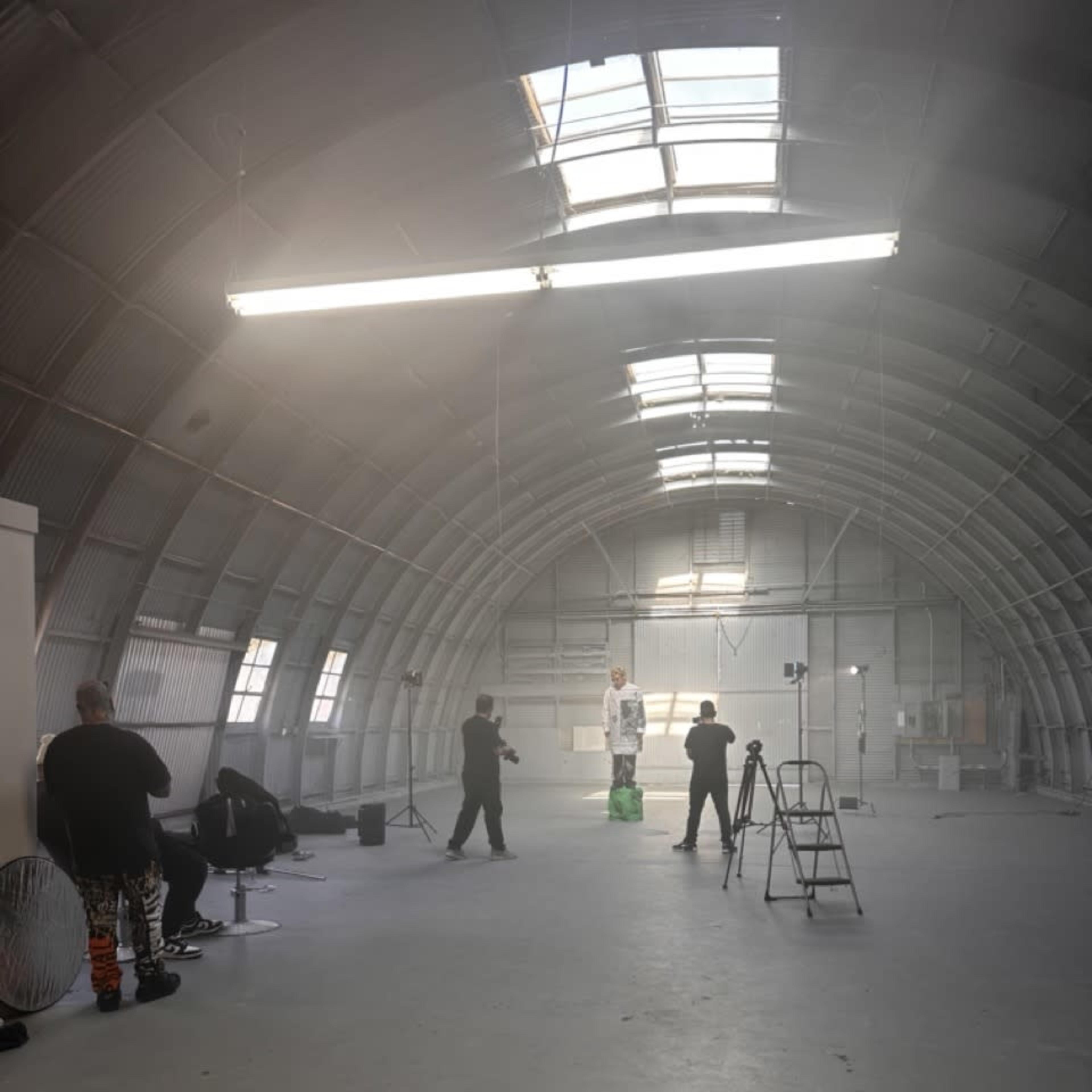 A group of people are setting up a photoshoot in a large, industrial space with a high, arched ceiling.