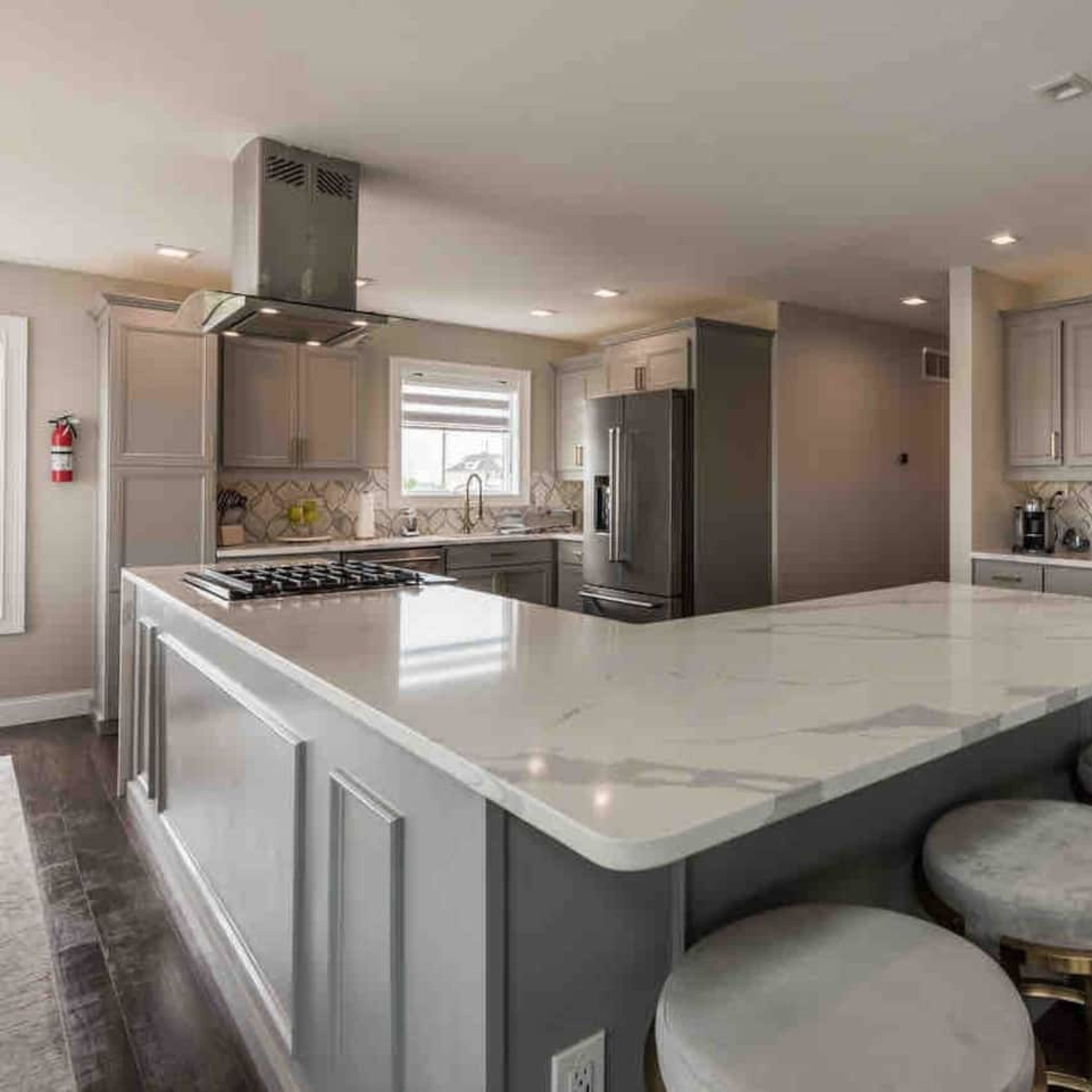 A modern kitchen with a large island featuring barstool seating, stainless steel appliances, and light-colored cabinetry.